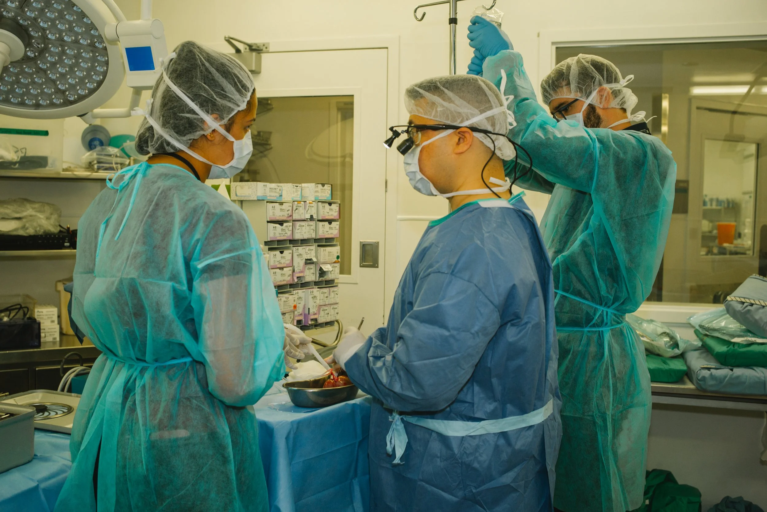 Group of medical professionals in scrubs, masks, and gloves performing surgery in an operating room.