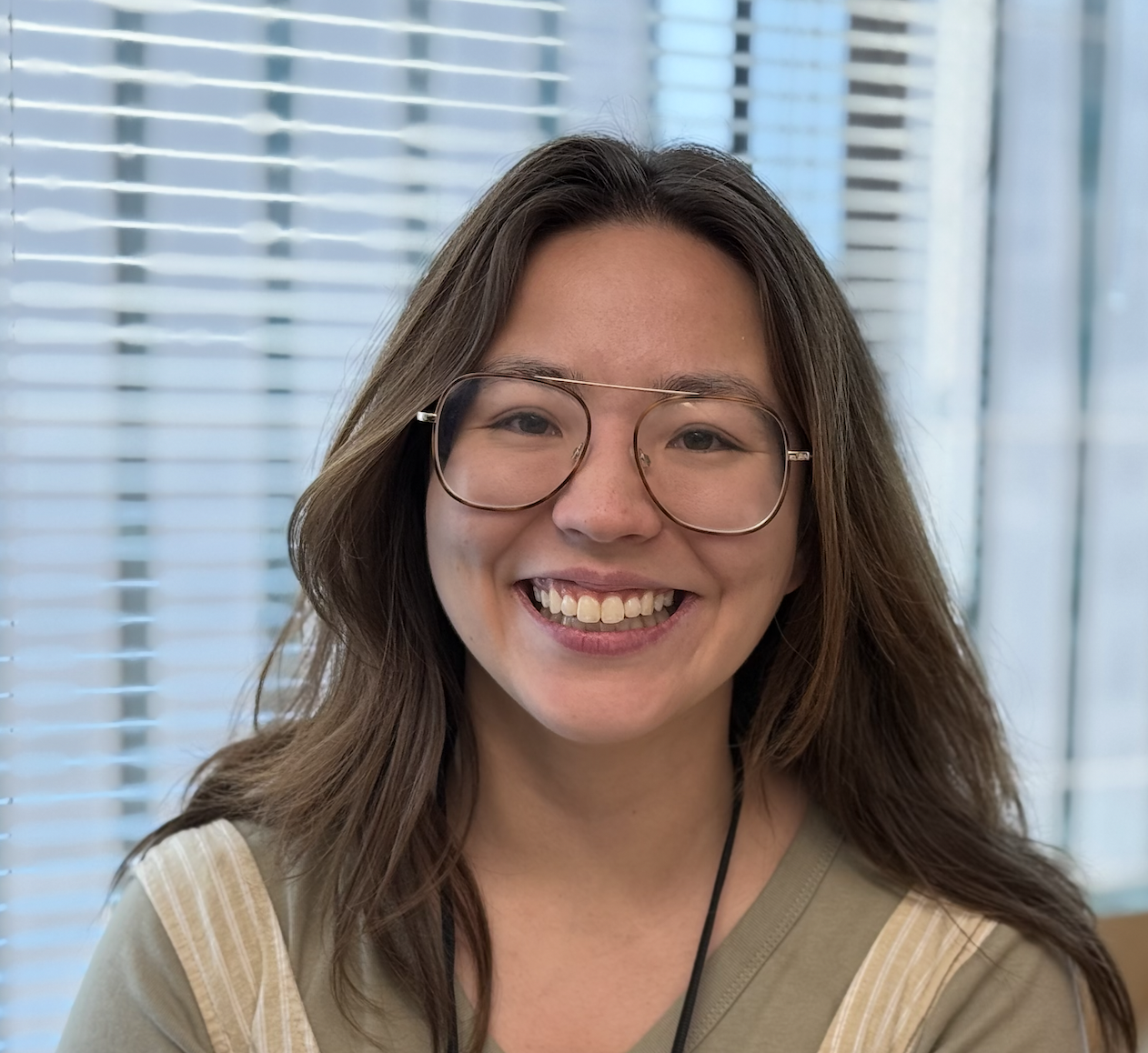 A woman with glasses and long brown hair smiling at the camera in a laboratory setting.