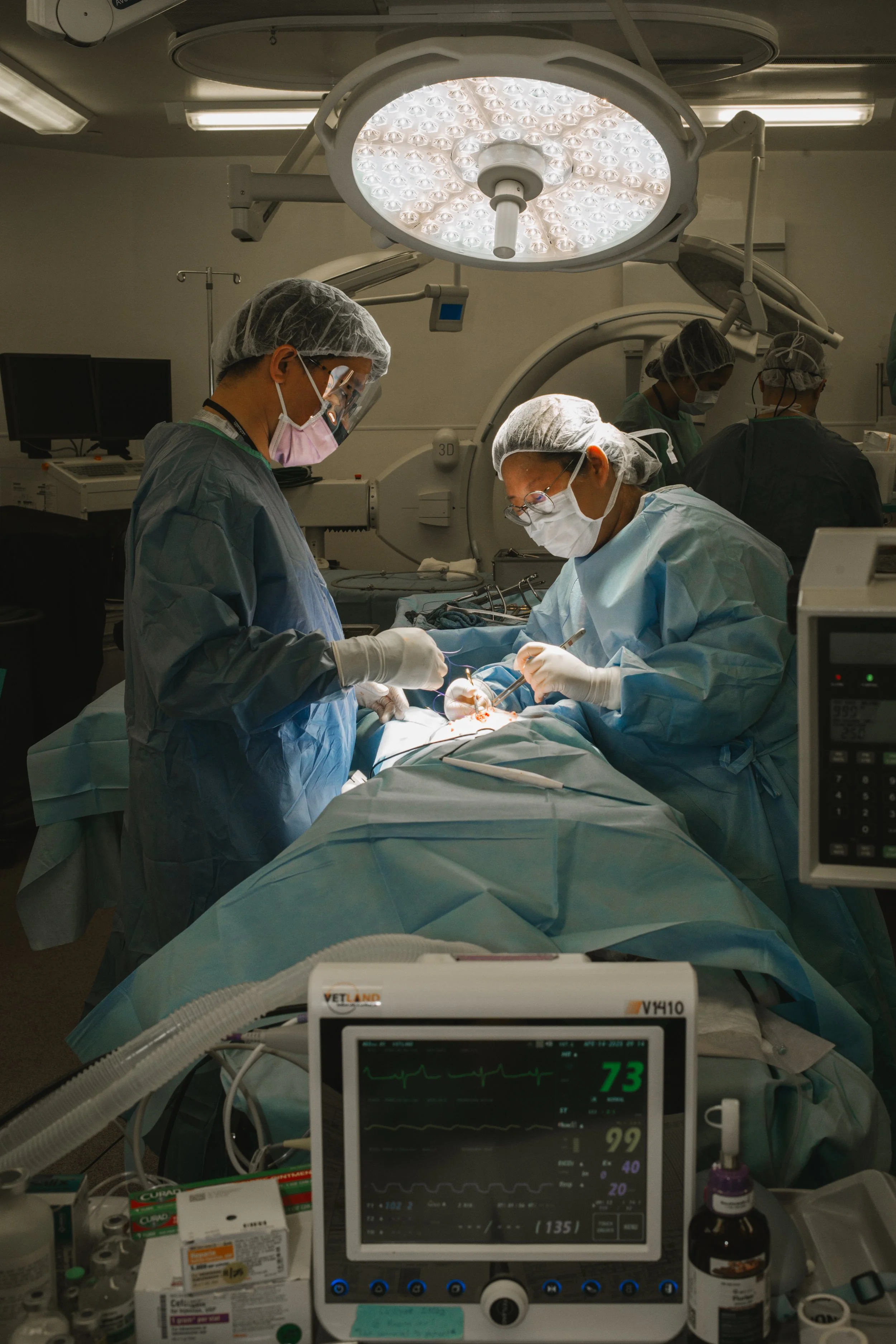 A team of surgeons performing an operation in an operating room, with surgical instruments, medical monitors, and bright surgical lights overhead.