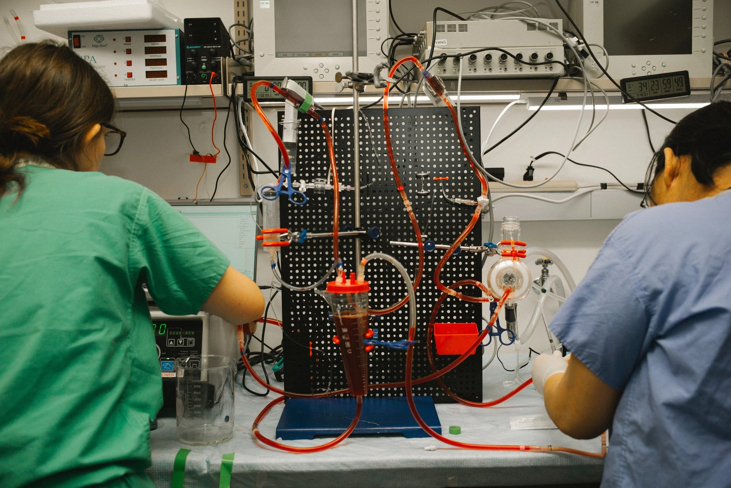 Two scientists working on an intricate laboratory setup with various tubes, wires, and equipment on a workbench.