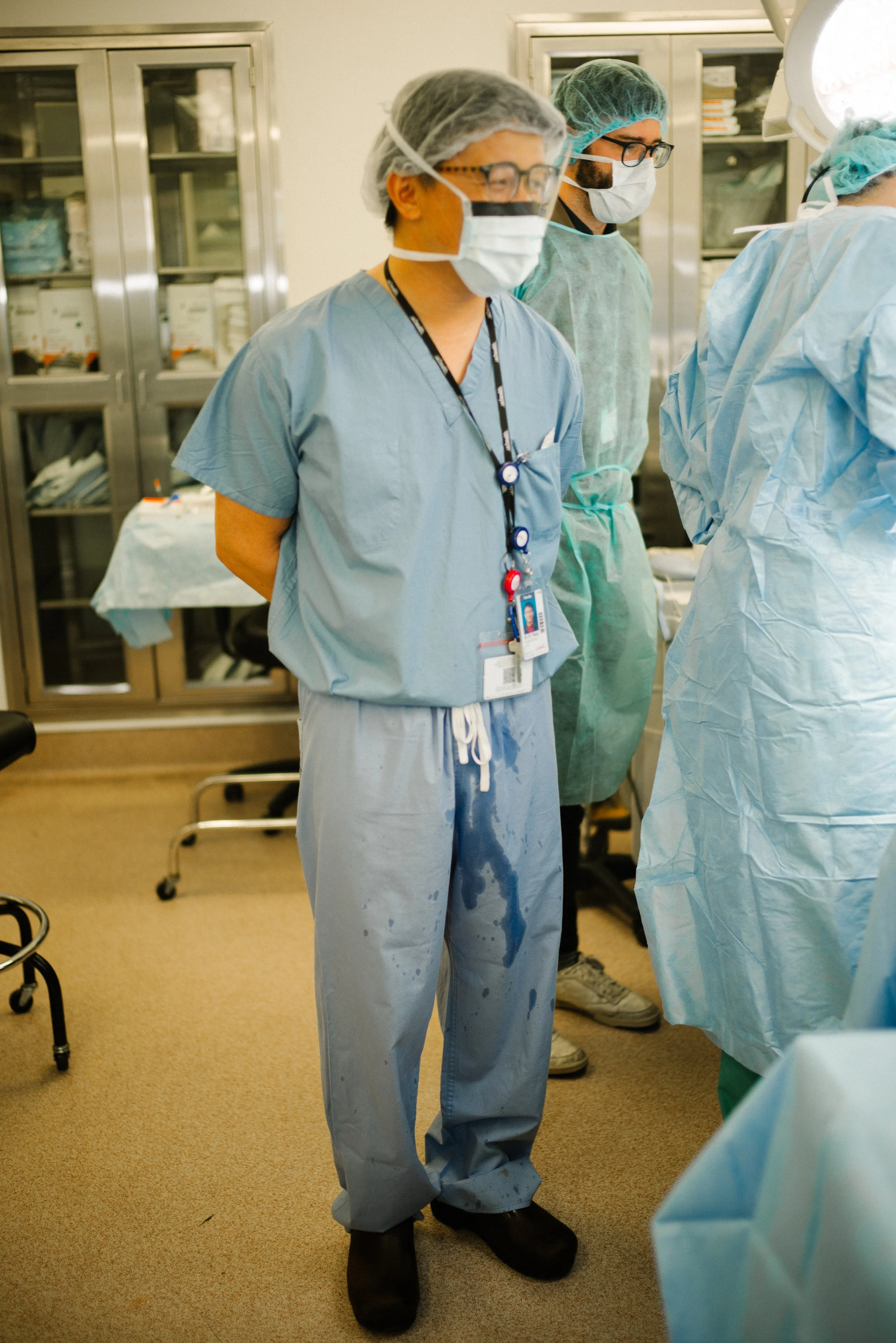 Medical team in surgical scrubs and masks standing in operating room with medical supplies.