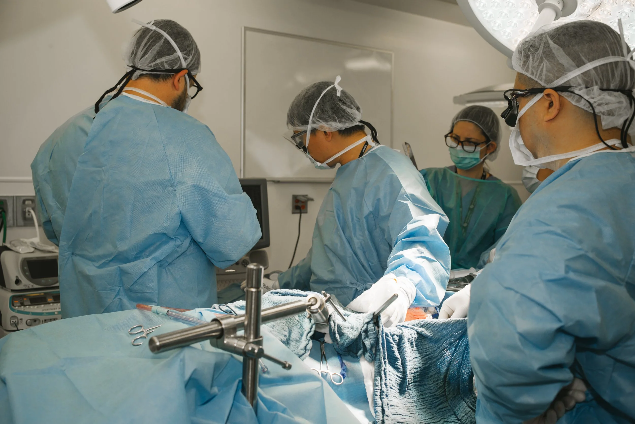 Medical team performing surgery in an operating room, dressed in scrubs, masks, and hair covers.