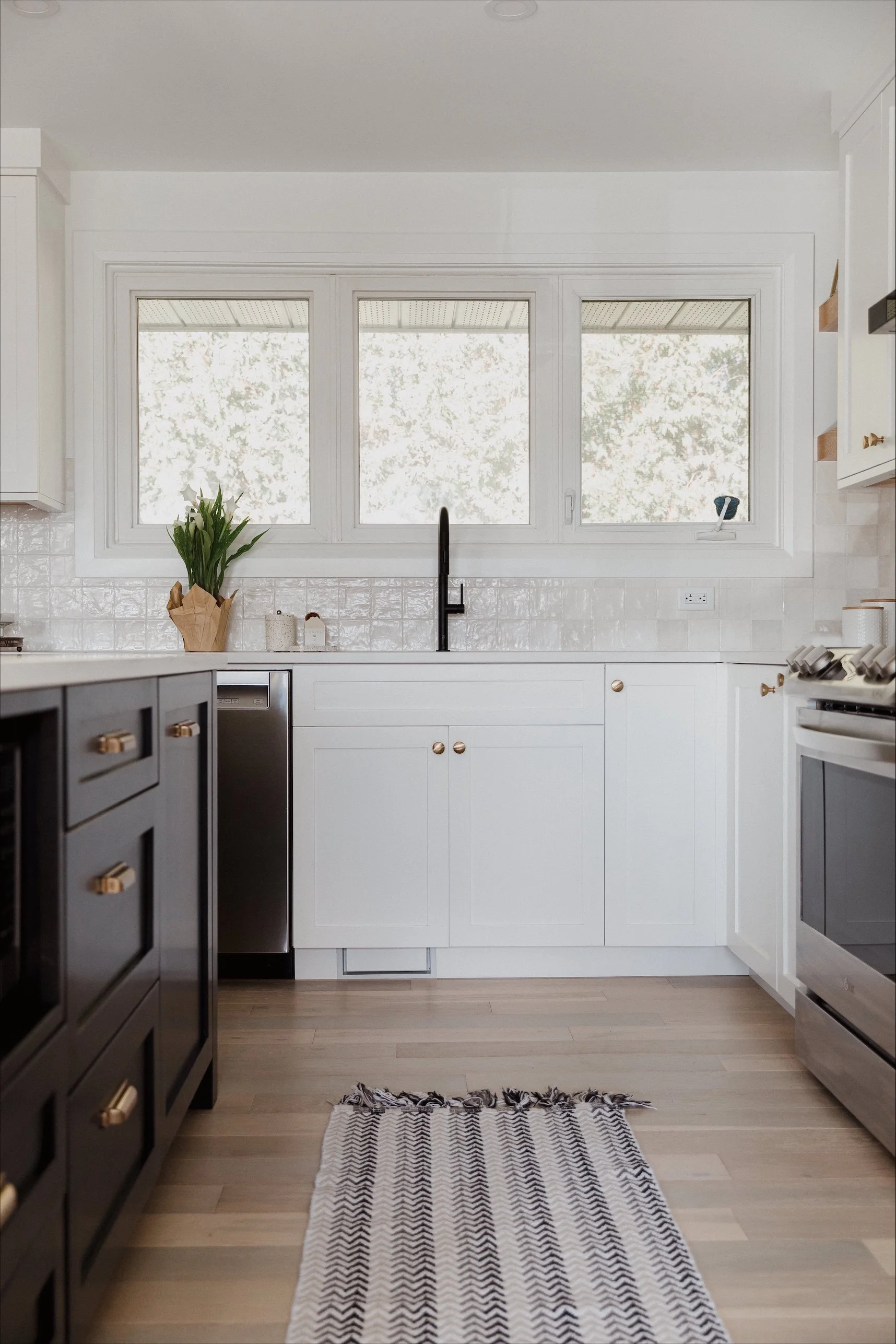 Decorative beige vase with lavender flowers, skincare products, and a spray bottle on a wooden tray, against a white wall with mirrors.