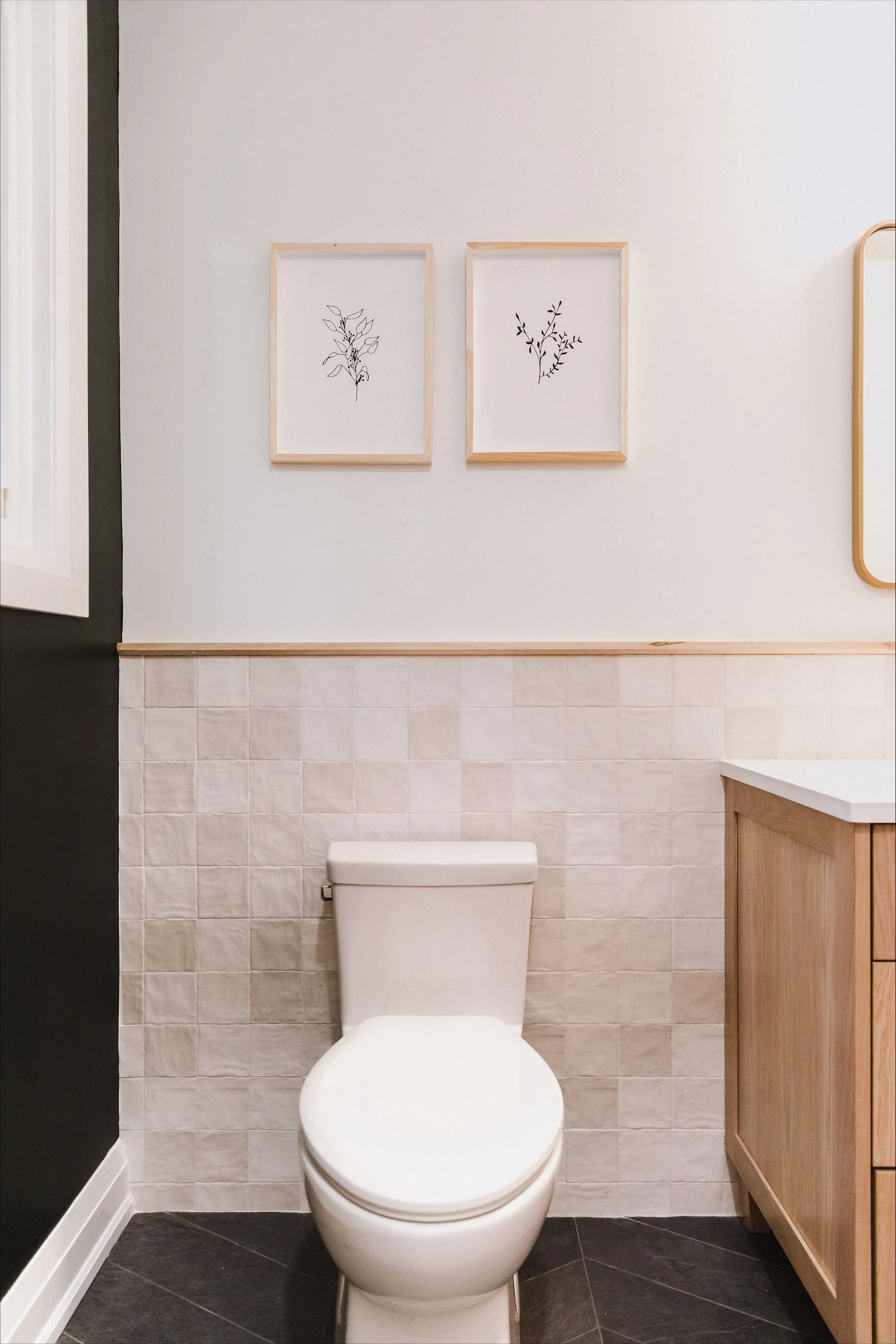 Bright modern bathroom featuring a double vanity with gold hardware, two large mirrors, and decorative items on the countertop. The bathroom has white walls, a textured floor, and minimalist framed artwork on the wall.