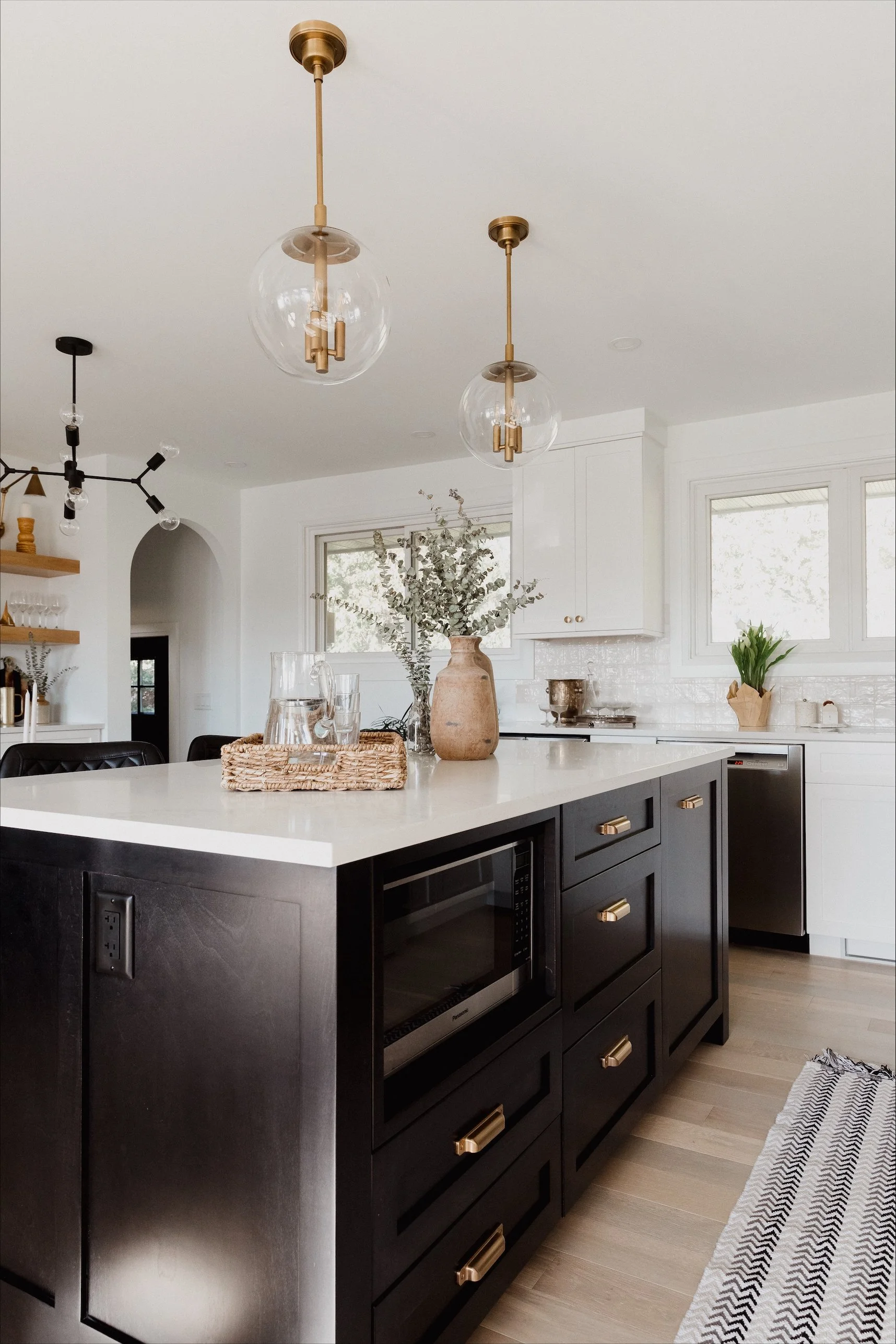 Bright modern bathroom featuring a double vanity with gold hardware, two large mirrors, and decorative items on the countertop. The bathroom has white walls, a textured floor, and minimalist framed artwork on the wall.