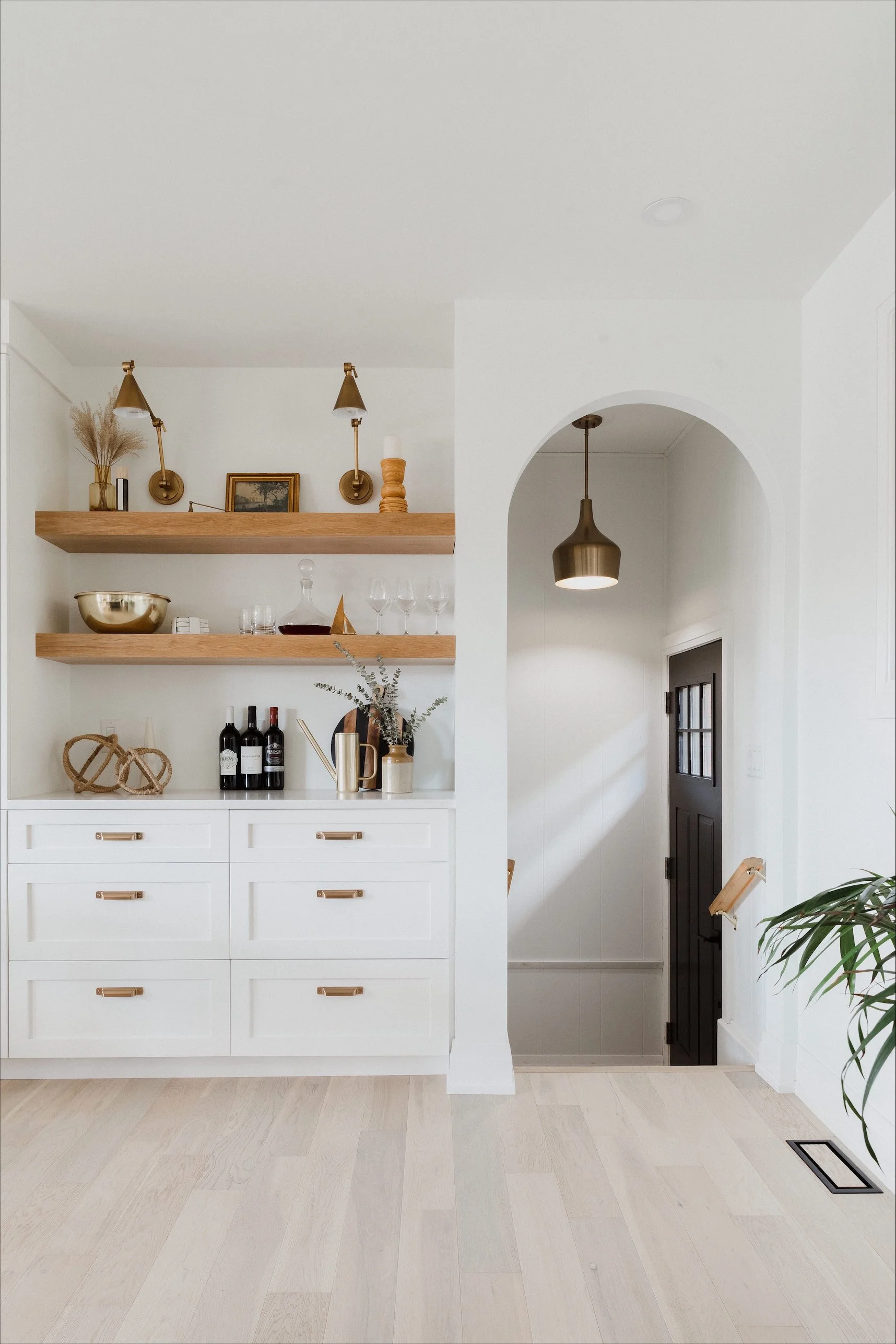 modern bathroom with a free-standing bathtub, glass-enclosed shower, two windows with blinds, a black ladder towel rack, a framed minimalist line art portrait on the wall, a small wooden stool, and decorative towels and plants.