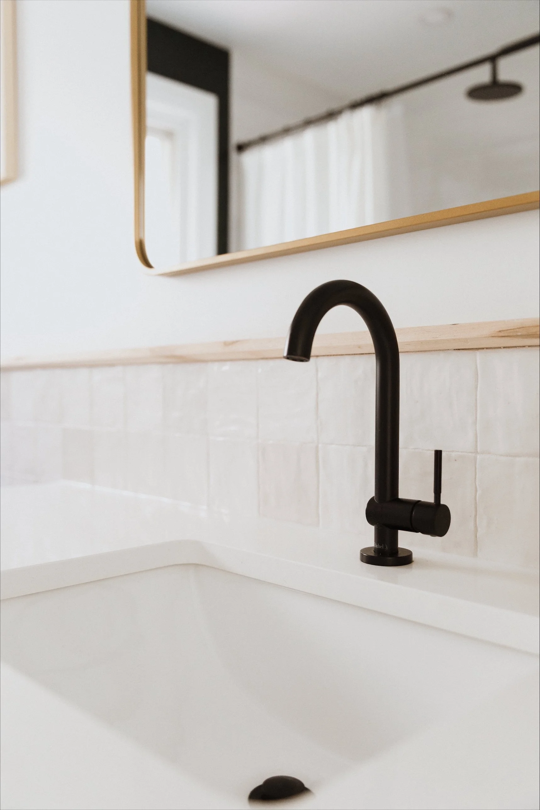 A cozy bathroom setting with a bathtub, a wicker basket filled with white towels and a bathrobe, slippers on the floor, a window, and a tray with a glass of white wine, a book, and a flower on the bathtub's edge.
