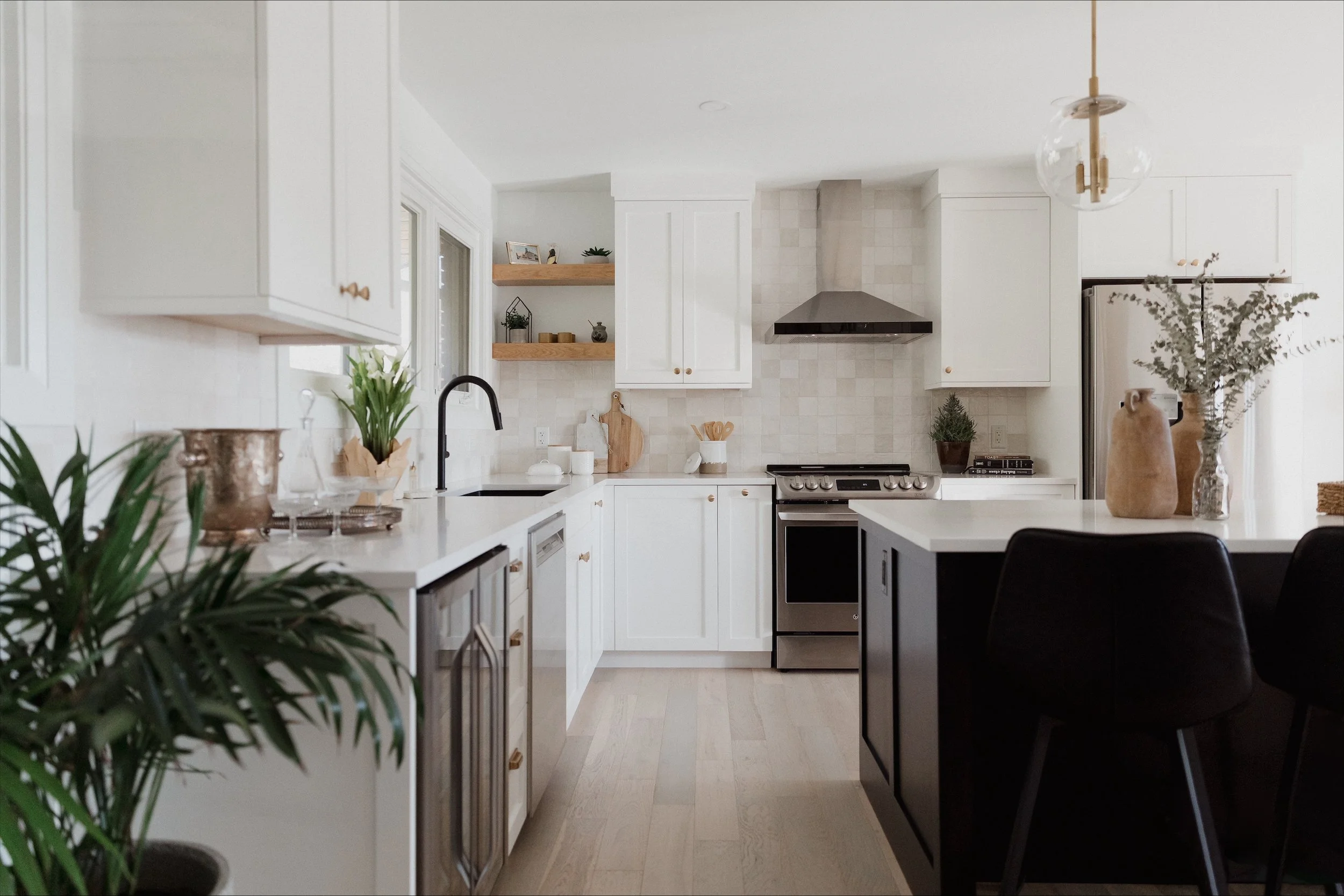White bathtub with brushed nickel faucet and handles, located in a bathroom with gray tiled wall and a window with white trim, with a green plant in a black metal basket nearby.