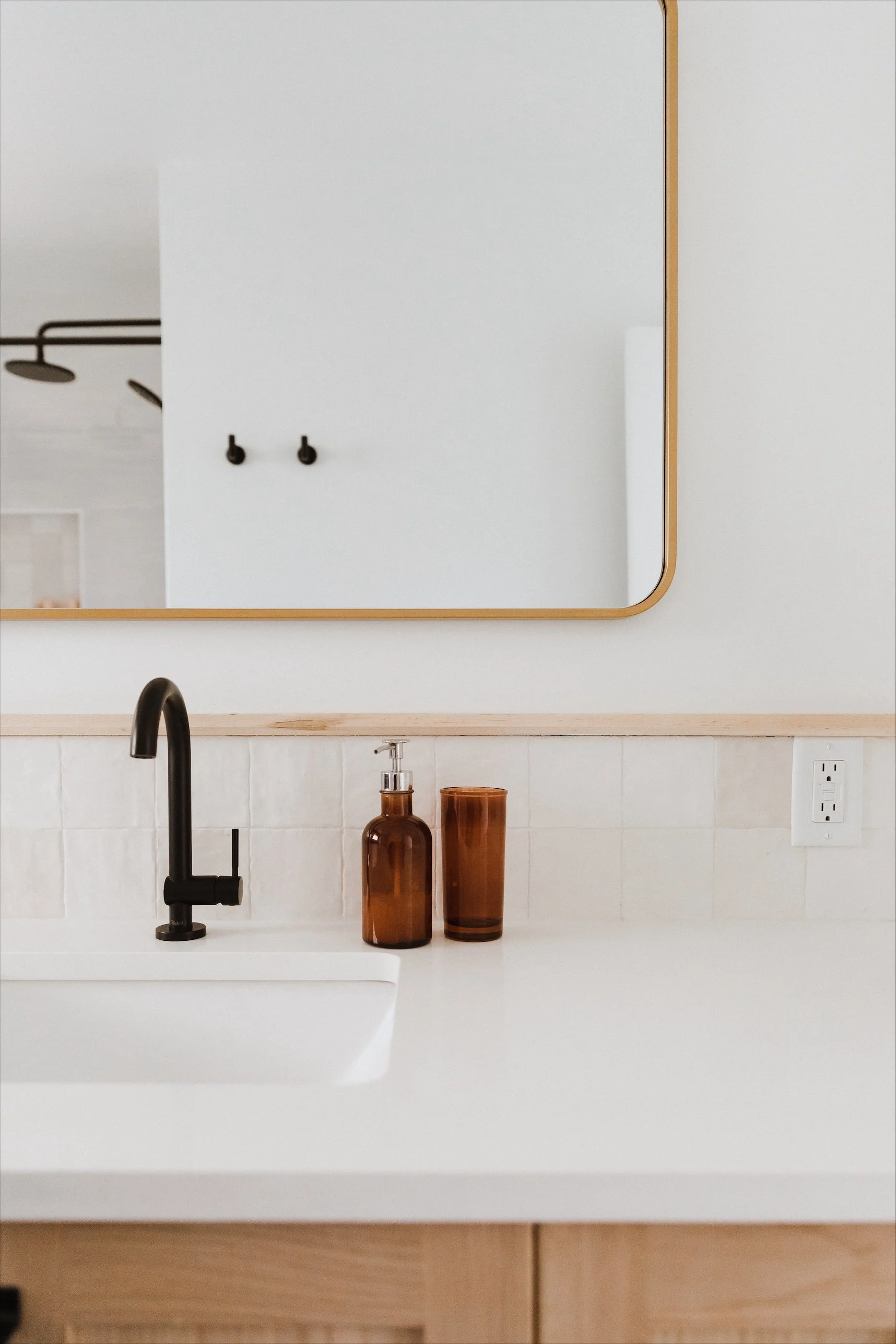 Bright bathroom with a white bathtub, glass-enclosed shower with a rain showerhead, and a window with white blinds. Decor includes a green plant, slippers, towels, a basket, and a wooden stool.