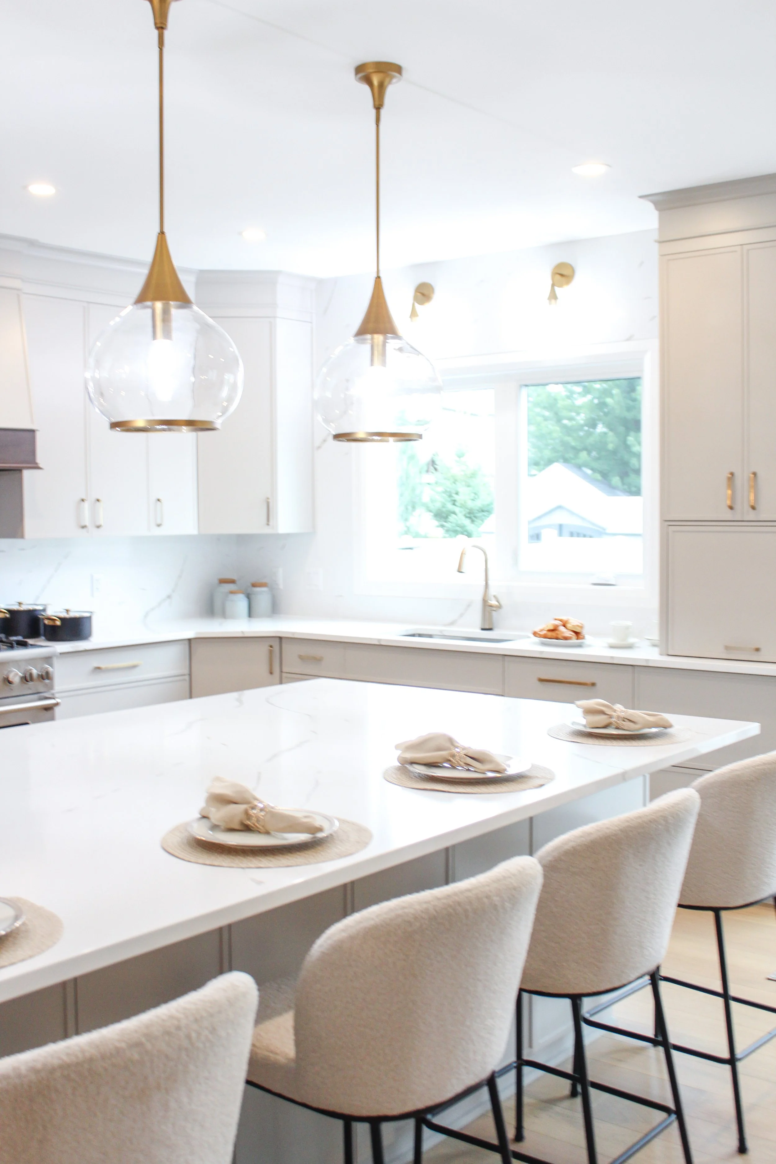 White kitchen with island, pendant lights, window, and chairs.