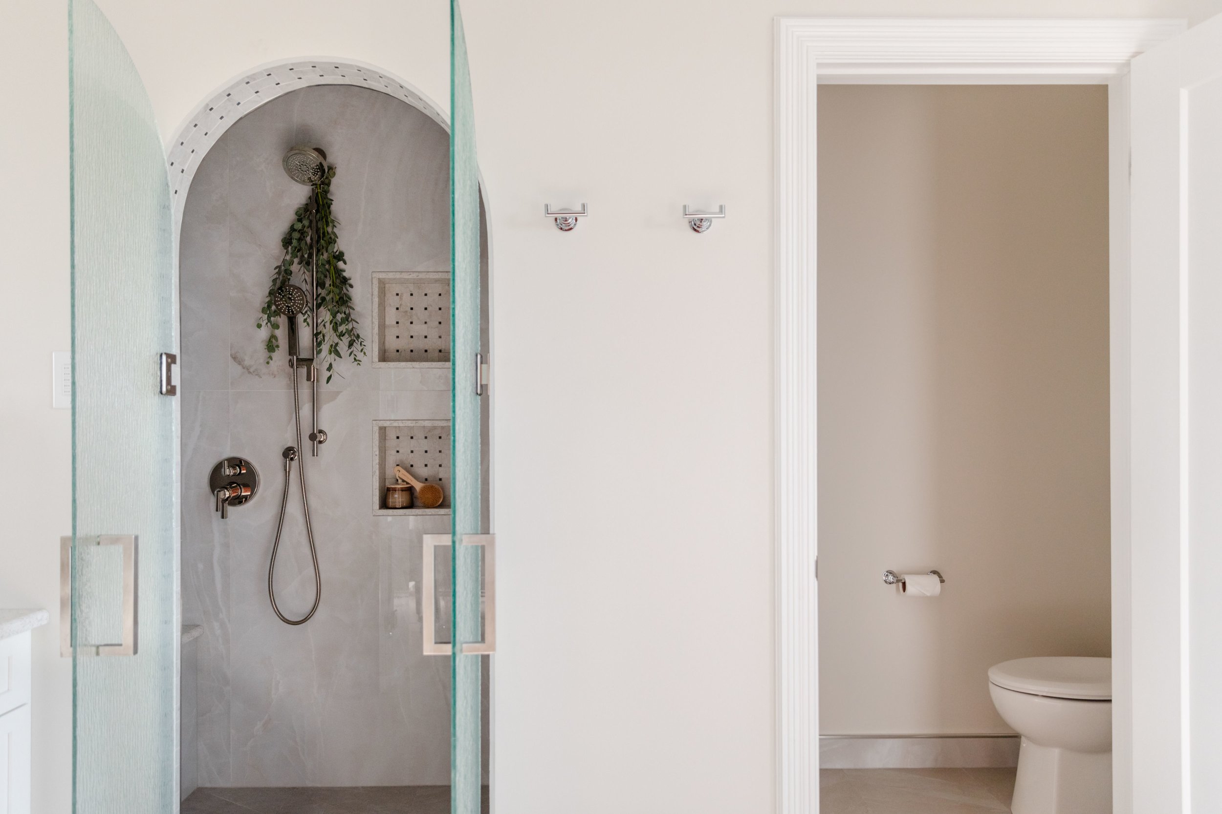 Bathroom with walk-in shower on the left and toilet stall on the right, separated by a wall with hooks.