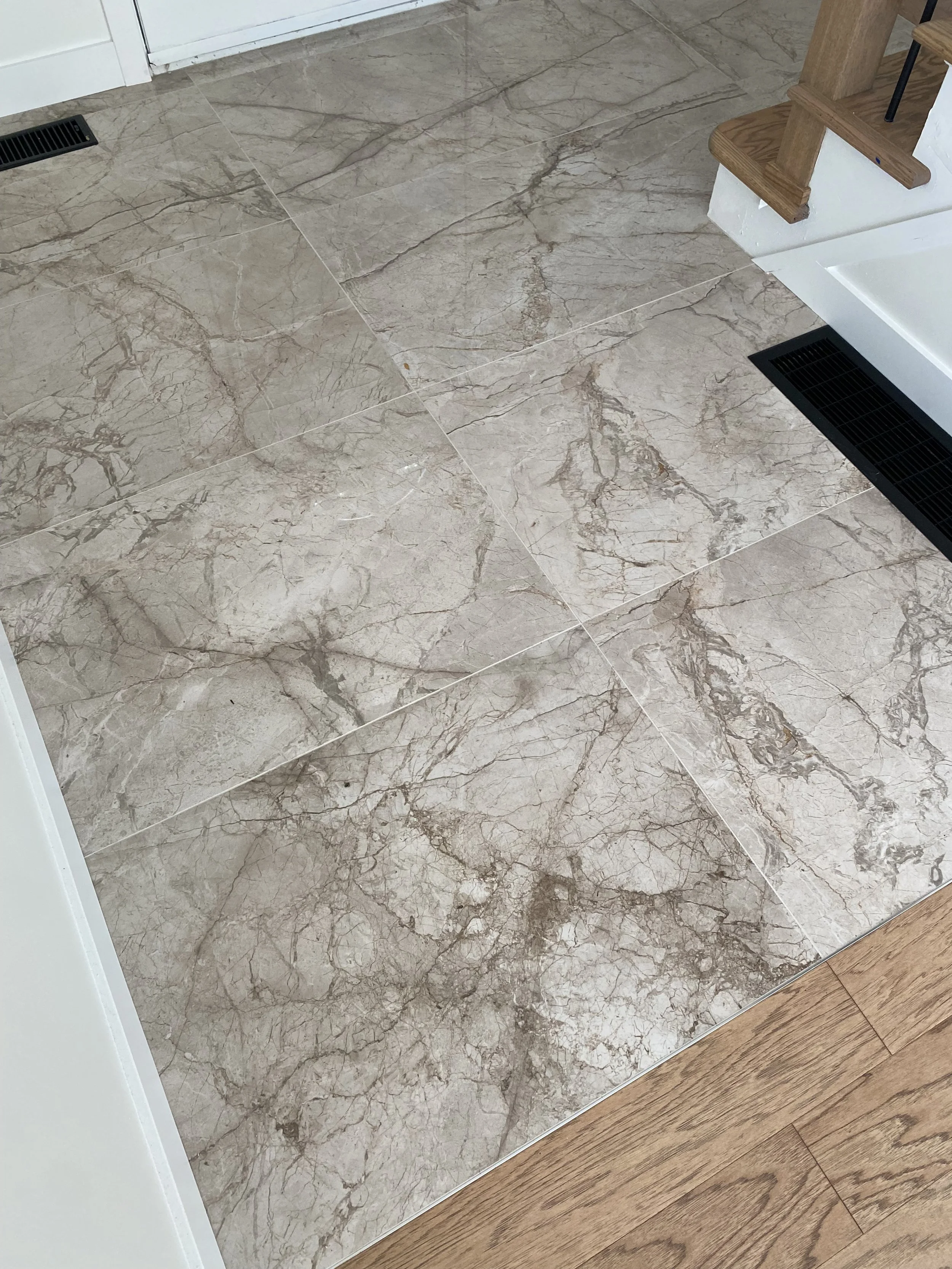 Modern bathroom with light-colored walls and flooring, featuring a large mirror above a white vanity with gold hardware, a bathtub with a glass partition, and a ladder towel rack near a window, decorated with minimalistic art and decor.