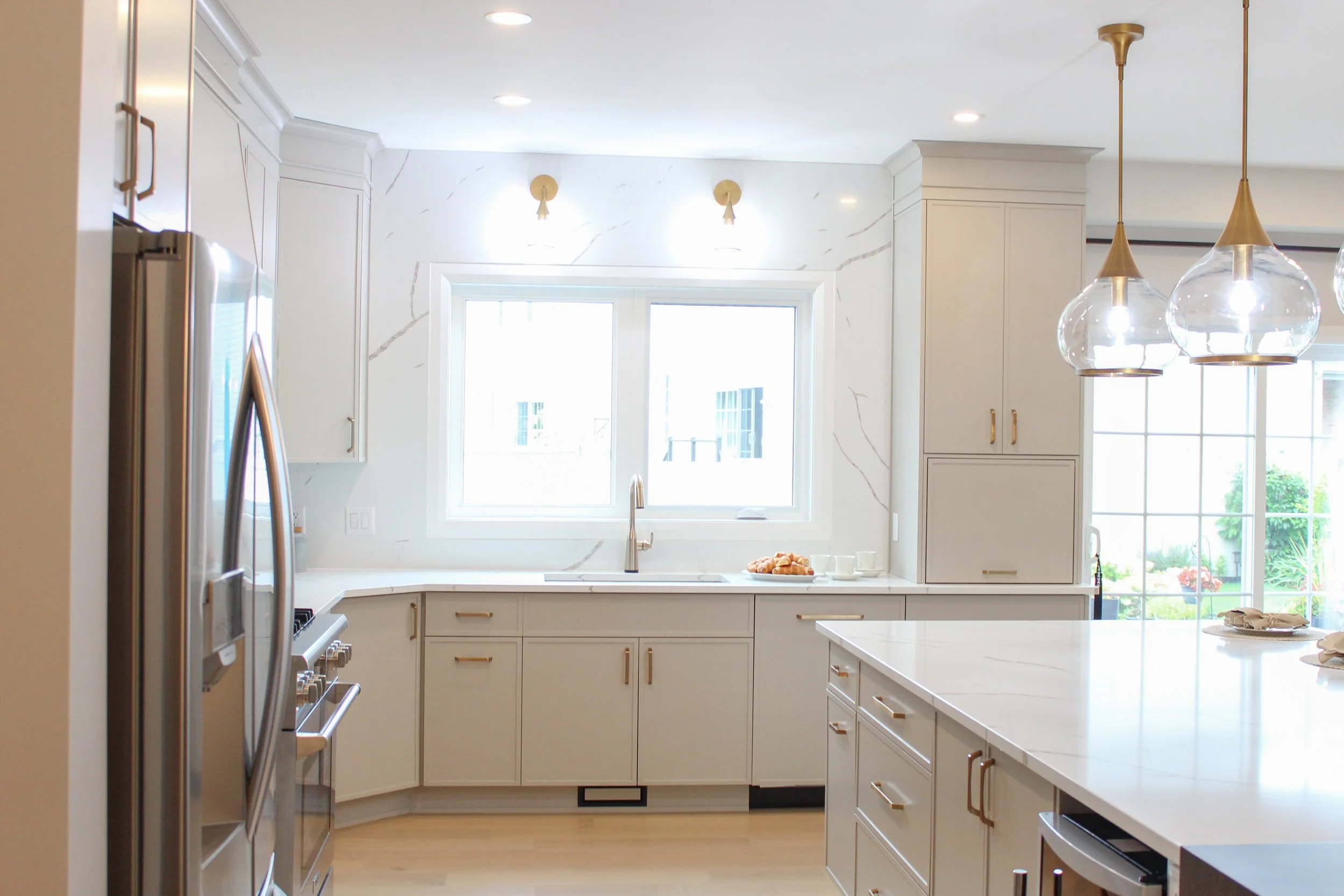 Modern kitchen with white cabinets, marble countertops, pendant lighting, and large window over the sink.