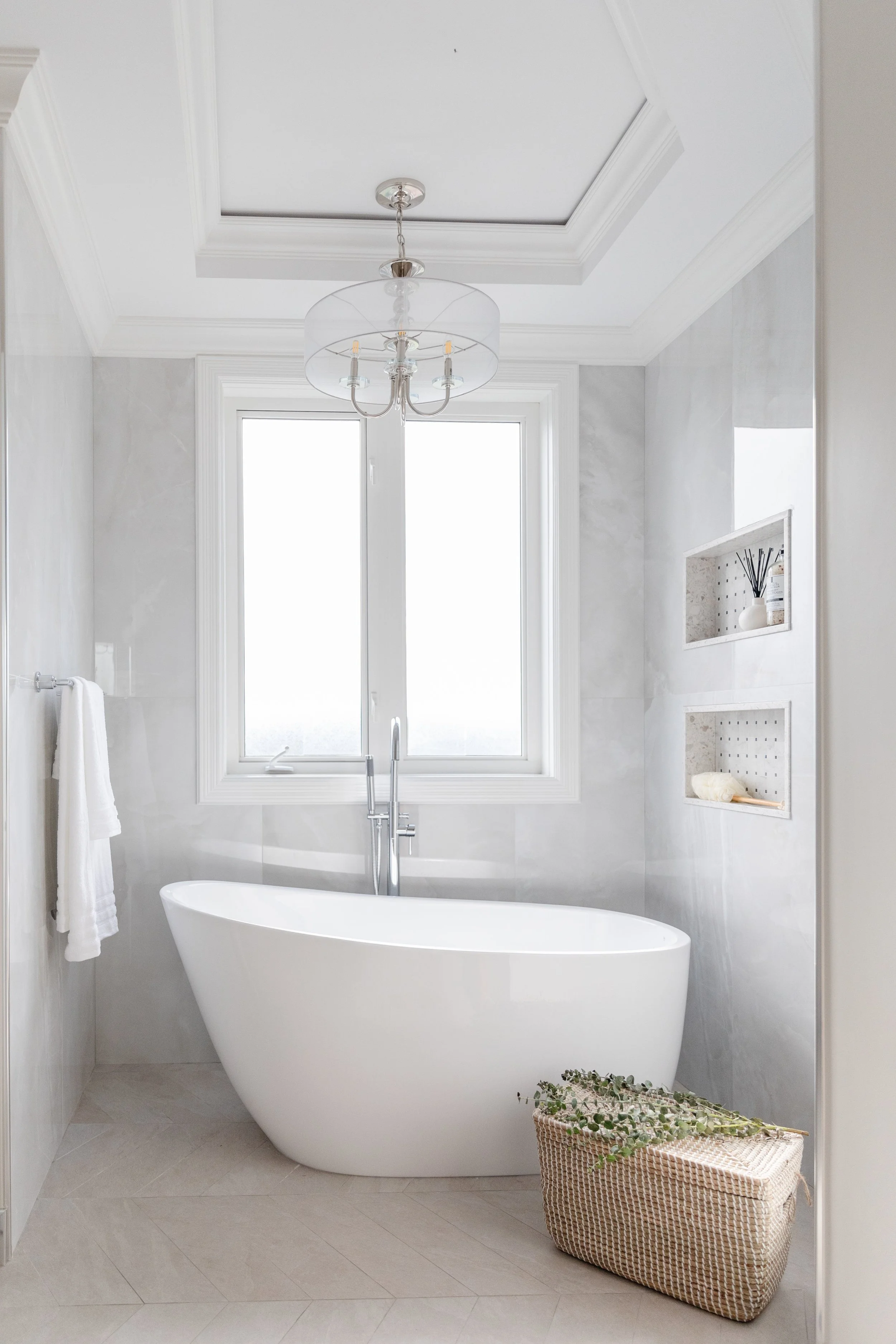 Modern white bathtub in a bright bathroom with large window, white walls, and built-in shelves.