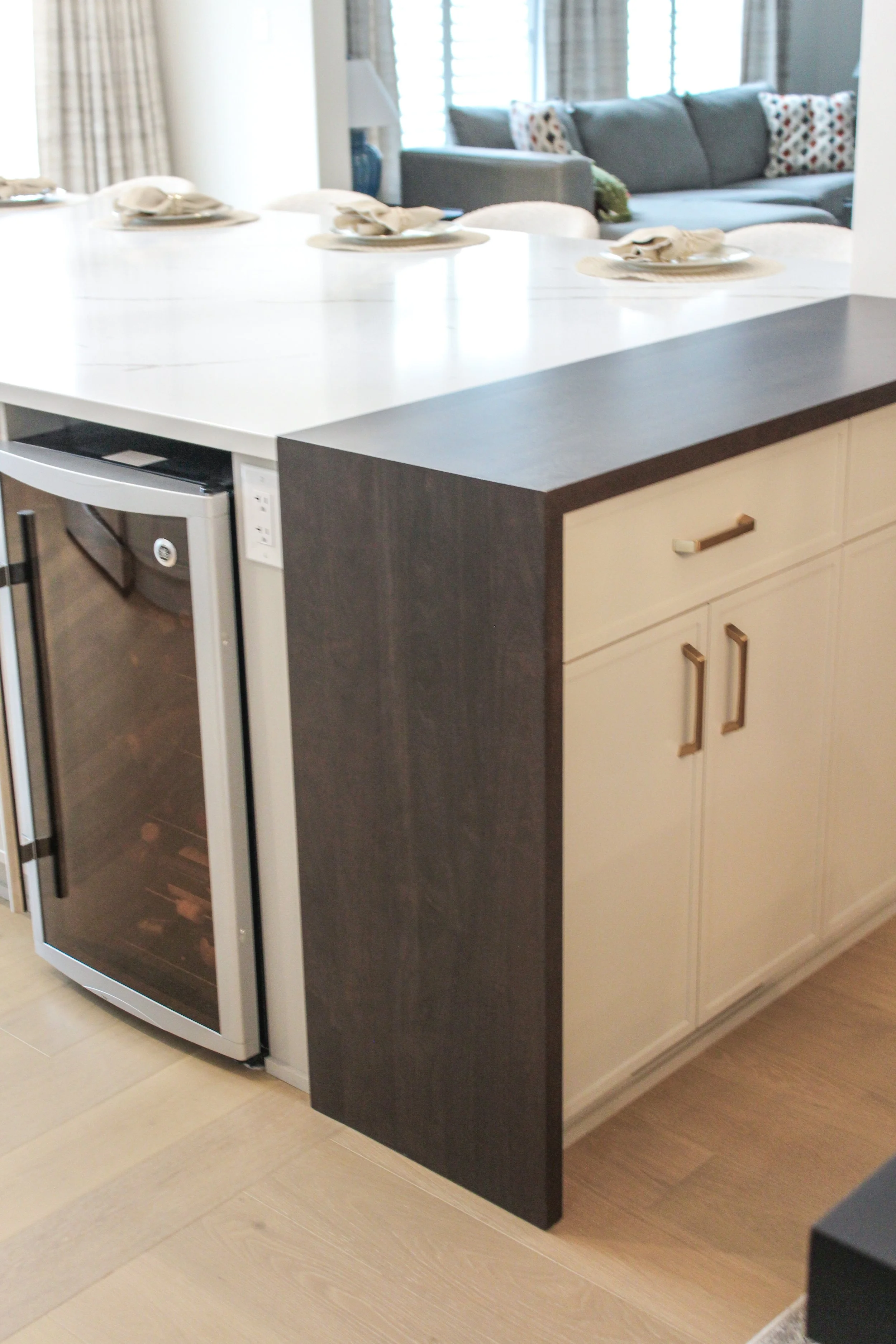 Kitchen island with a wine cooler, dark and light cabinetry, and a white countertop with place settings.