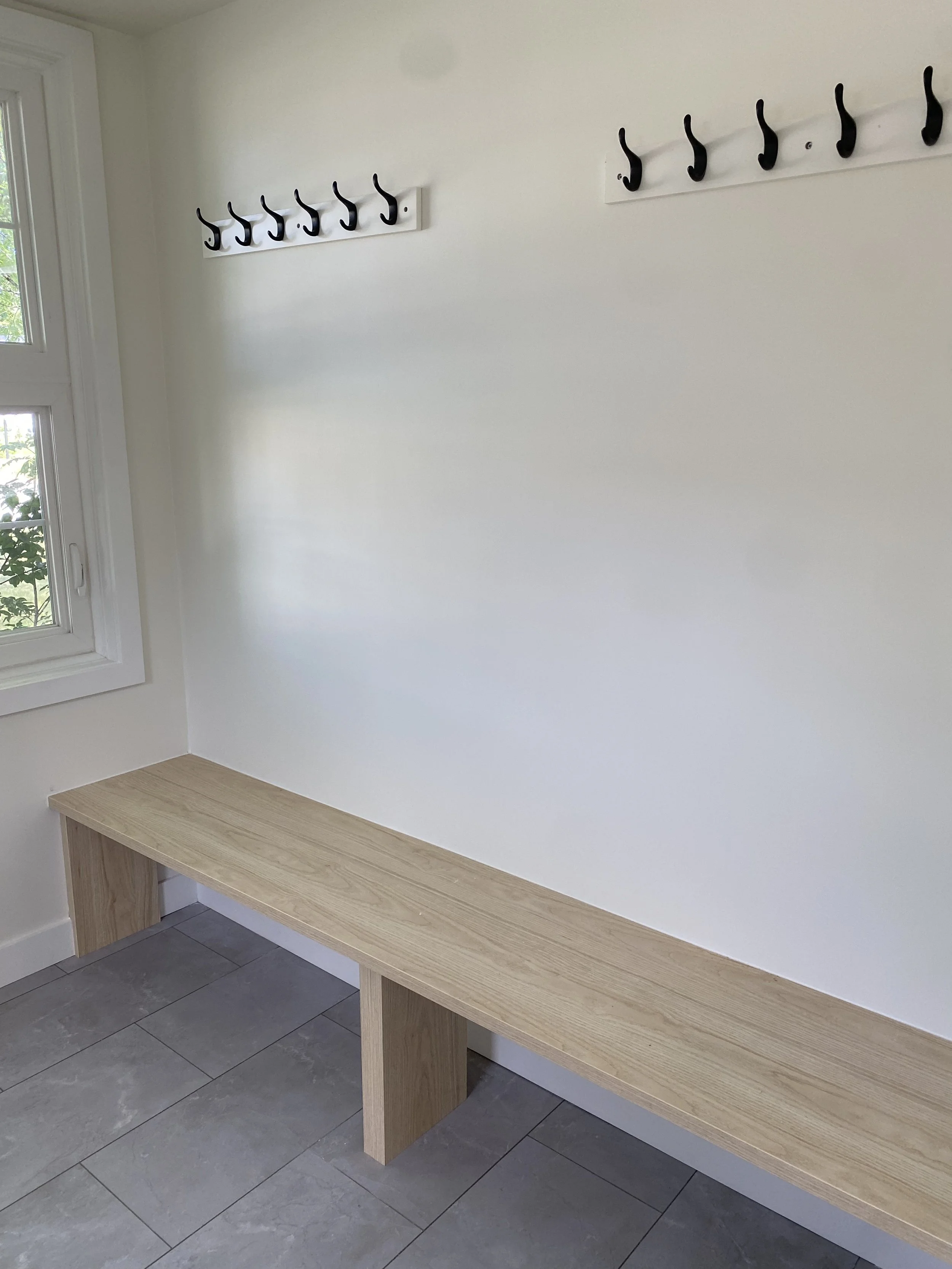 Bright modern bathroom featuring a double vanity with gold hardware, two large mirrors, and decorative items on the countertop. The bathroom has white walls, a textured floor, and minimalist framed artwork on the wall.