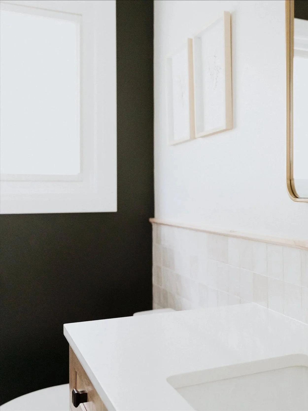 A modern bathroom with a double vanity, two mirrors, gold fixtures, and light fixtures on each side of the mirrors. The vanity has grey cabinets and a white countertop, with decor and toiletries on it.