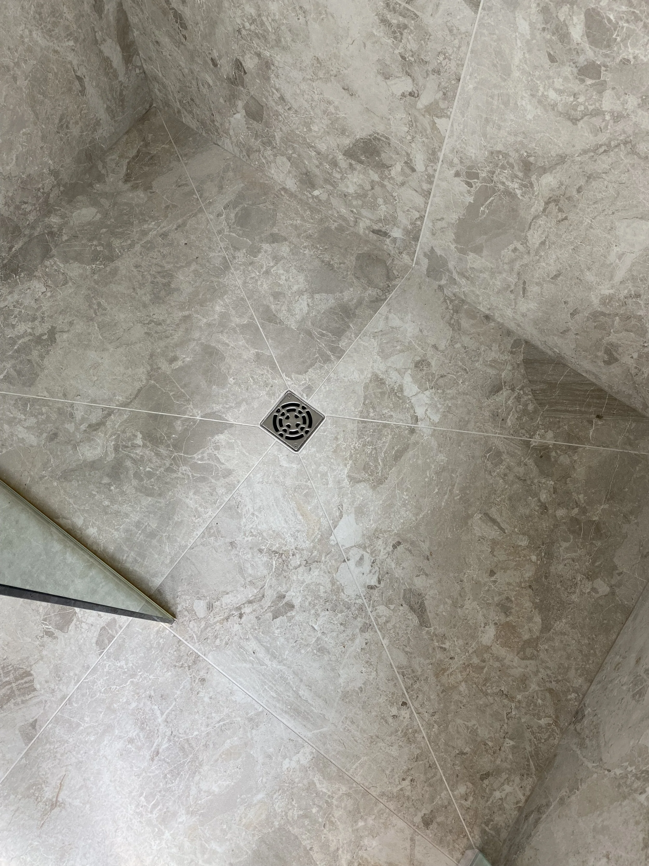 Close-up of a modern wall sconce with a brass finish and ribbed glass shade mounted on a white wall near a mirror in a bathroom.