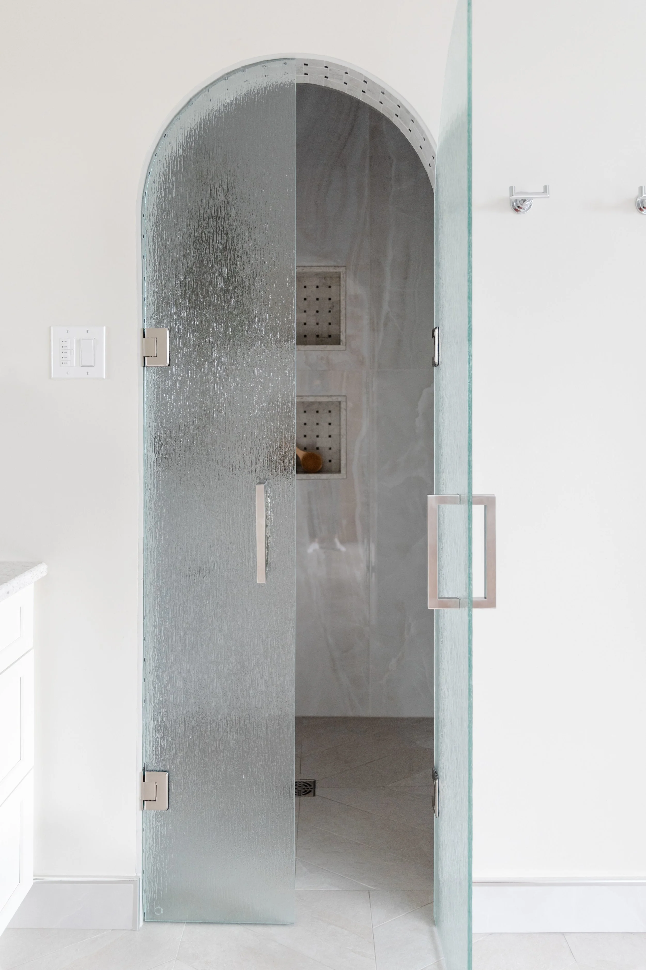 A frosted glass shower door with arched top in a modern bathroom, featuring marble tiles and built-in niches.