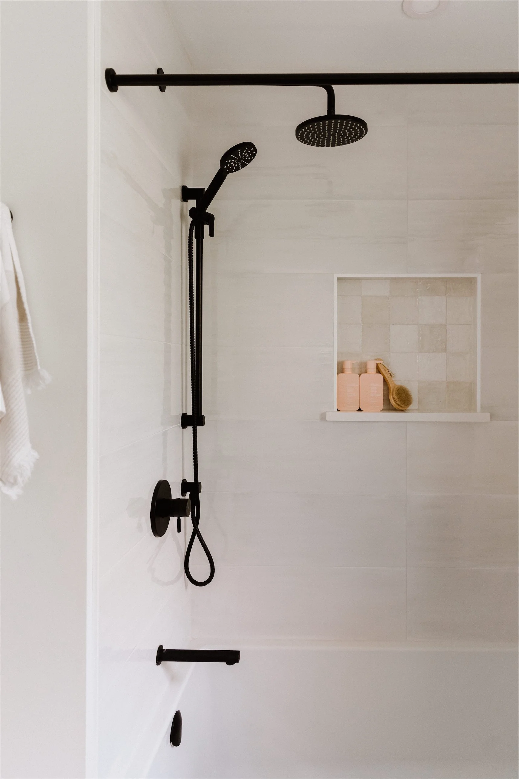 Shower with a brass shower head and fixtures, a built-in shelf with toiletries, a hanging plant, and a small wooden stool in a modern bathroom with light gray marble walls.