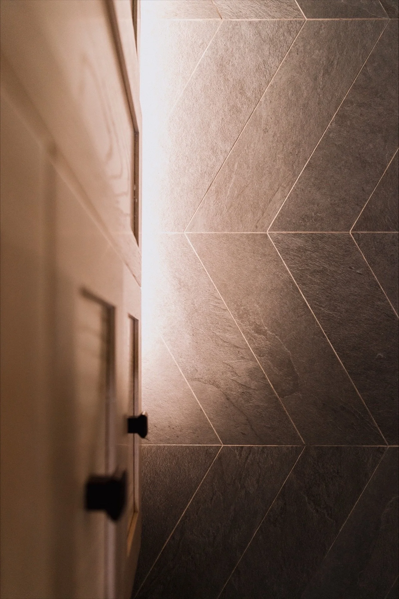 modern bathroom with a free-standing bathtub, glass-enclosed shower, two windows with blinds, a black ladder towel rack, a framed minimalist line art portrait on the wall, a small wooden stool, and decorative towels and plants.
