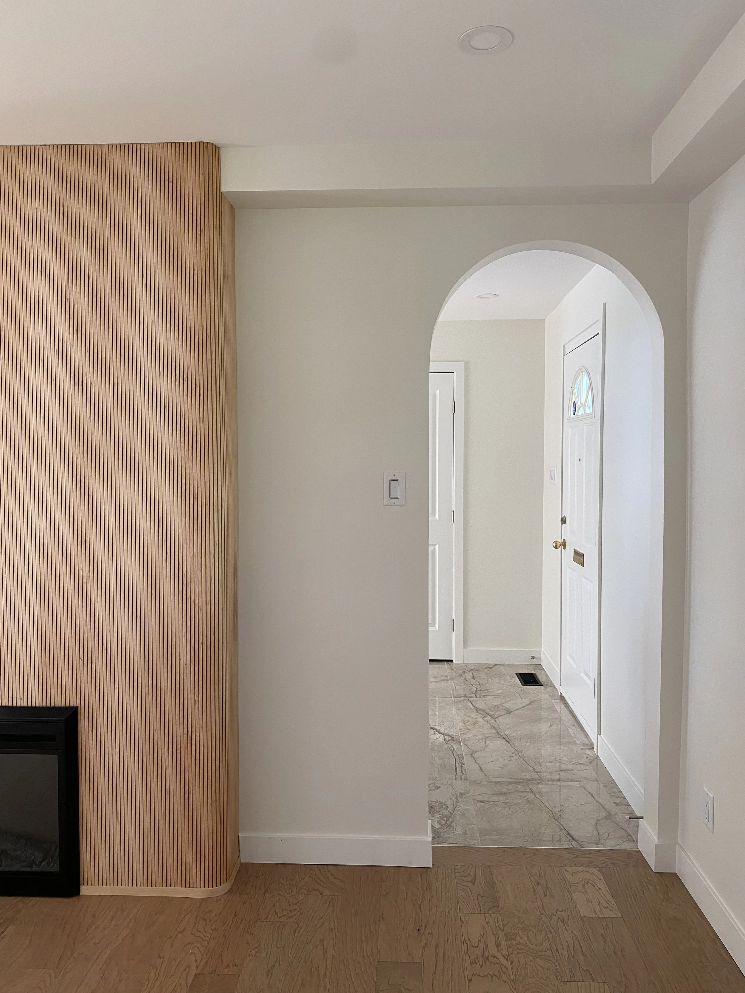 A minimalist bathroom with white walls, a white toilet with a decorative vase with black branches on top, a white textured wastebasket, and part of a vanity with drawers, a mirror, and a wall-mounted light fixture.