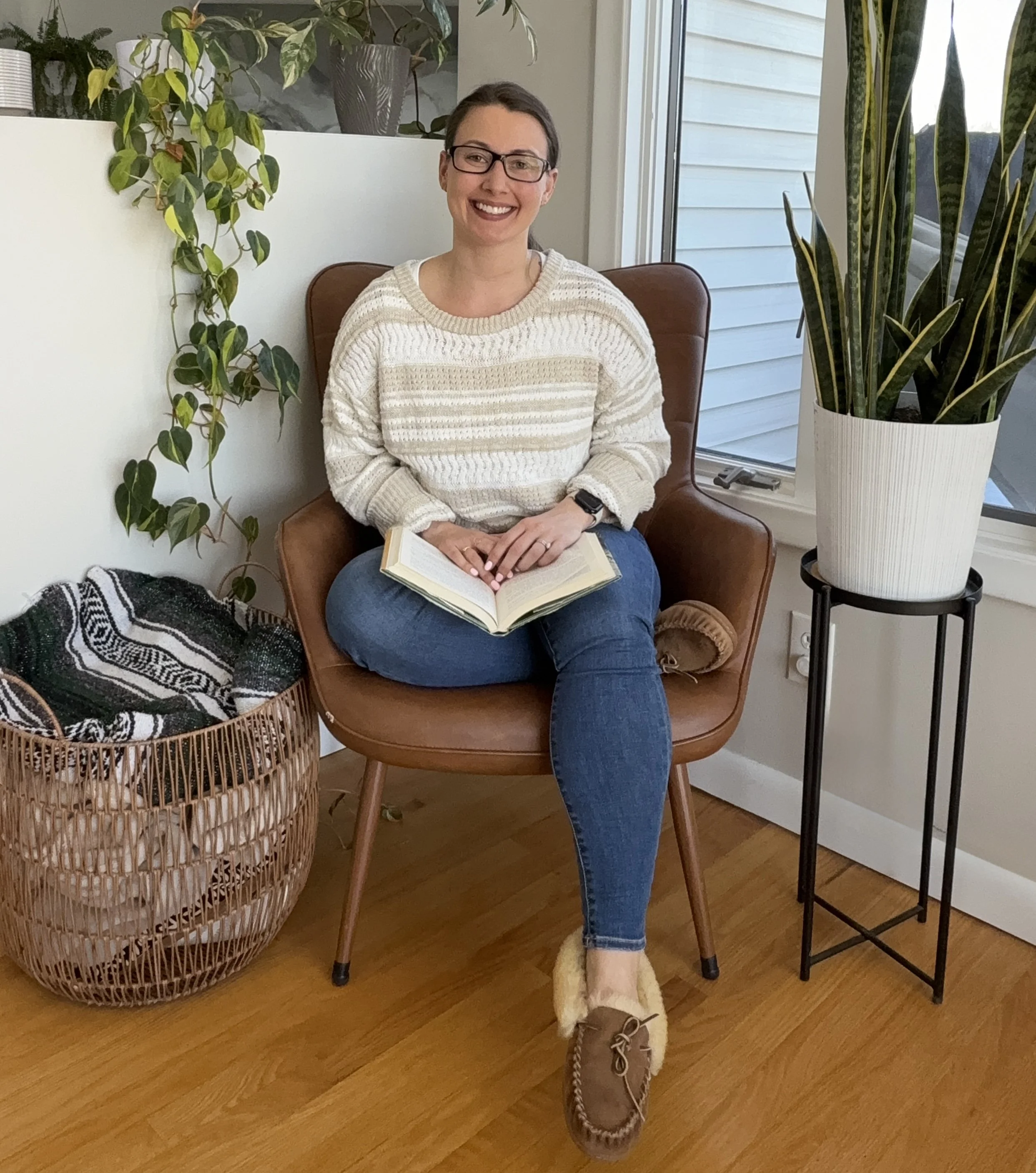 Amberleigh Maida seated in a warm, calming office space, smiling and ready to support clients through pain reprocessing therapy and life coaching.