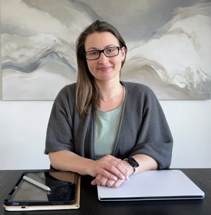 Amberleigh Maida sitting at her desk in a professional office setting, outlining her structured and supportive approach to pain reprocessing therapy and life coaching.