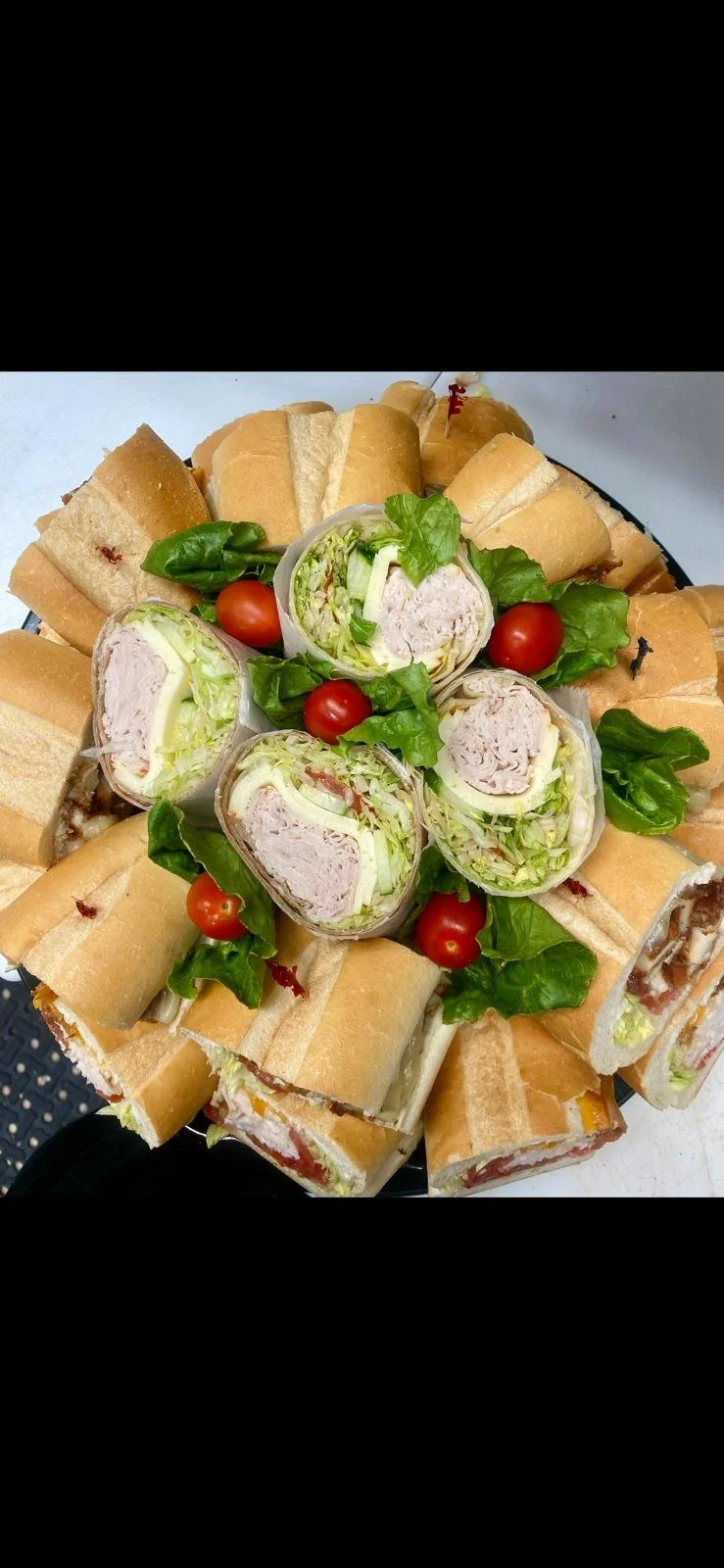 Plate with assorted sandwiches, some cut into halves or quarters, surrounded by cherry tomatoes and fresh green lettuce leaves.