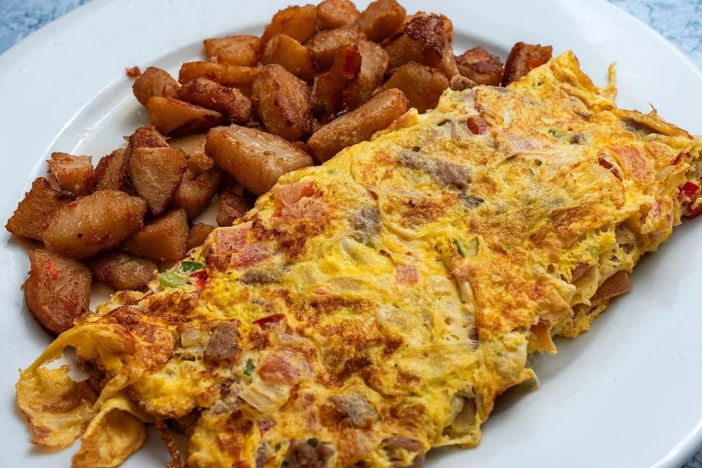 A plate with a scrambled omelette containing ham, mushrooms, and green peppers, served alongside fried diced potatoes.