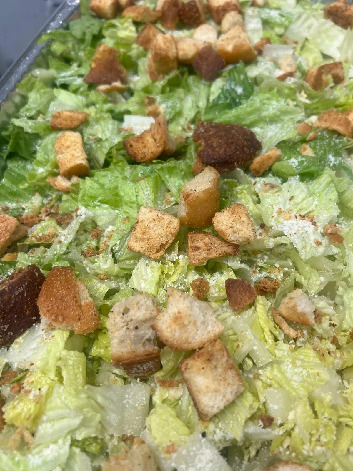 Close-up of a Caesar salad with chopped romaine lettuce, croutons, grated cheese, and a creamy dressing.