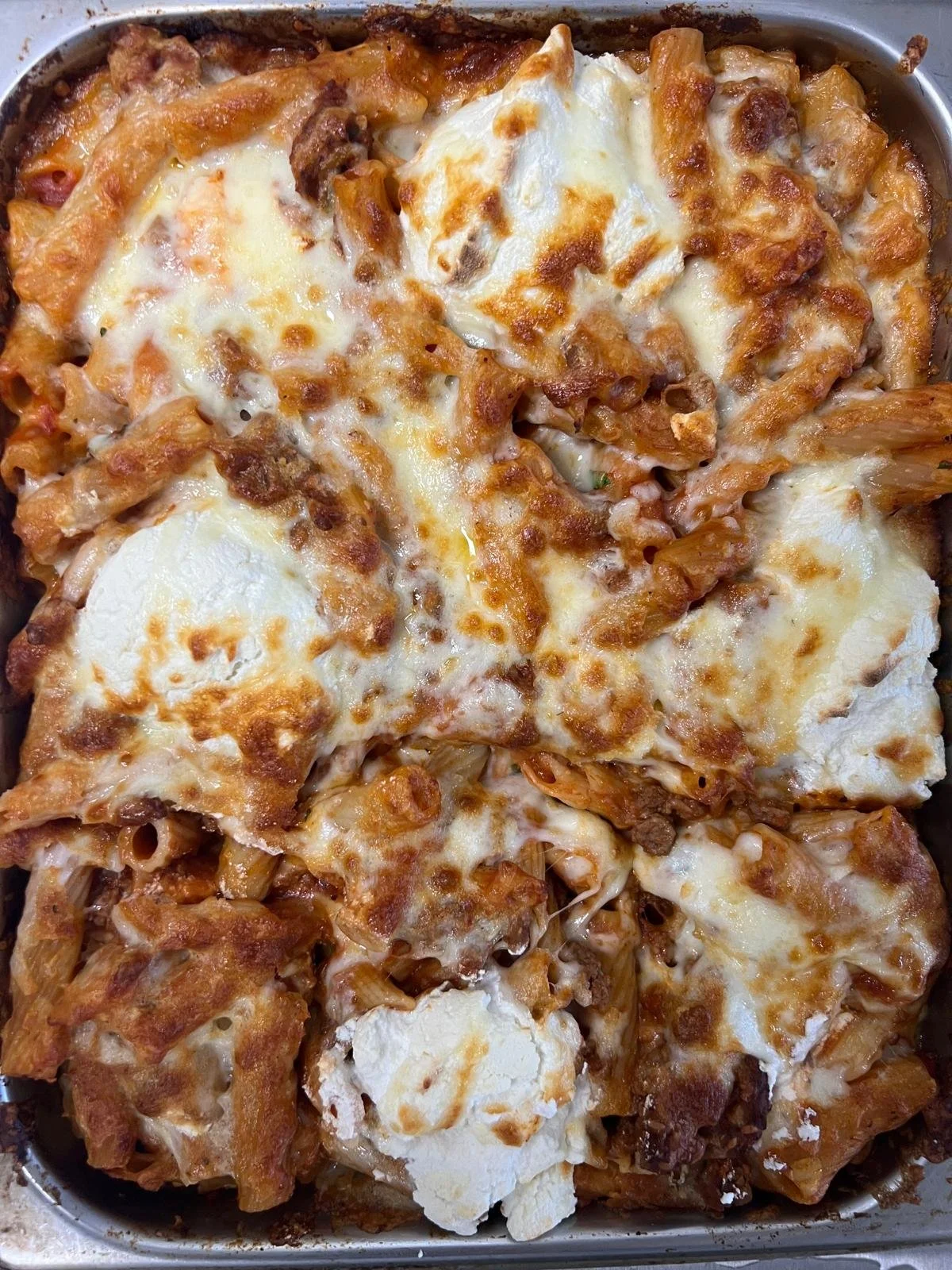 Baked casserole dish with layers of melted cheese, baked eggs, and possibly pasta or meat, topped with browned cheese.