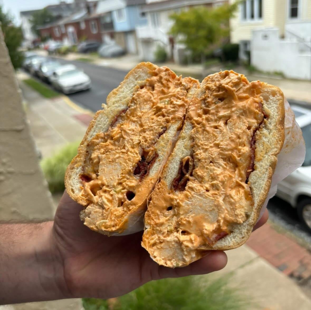 A hand holding a peanut butter and jelly sandwich on bread, with a residential street and parked cars in the background.