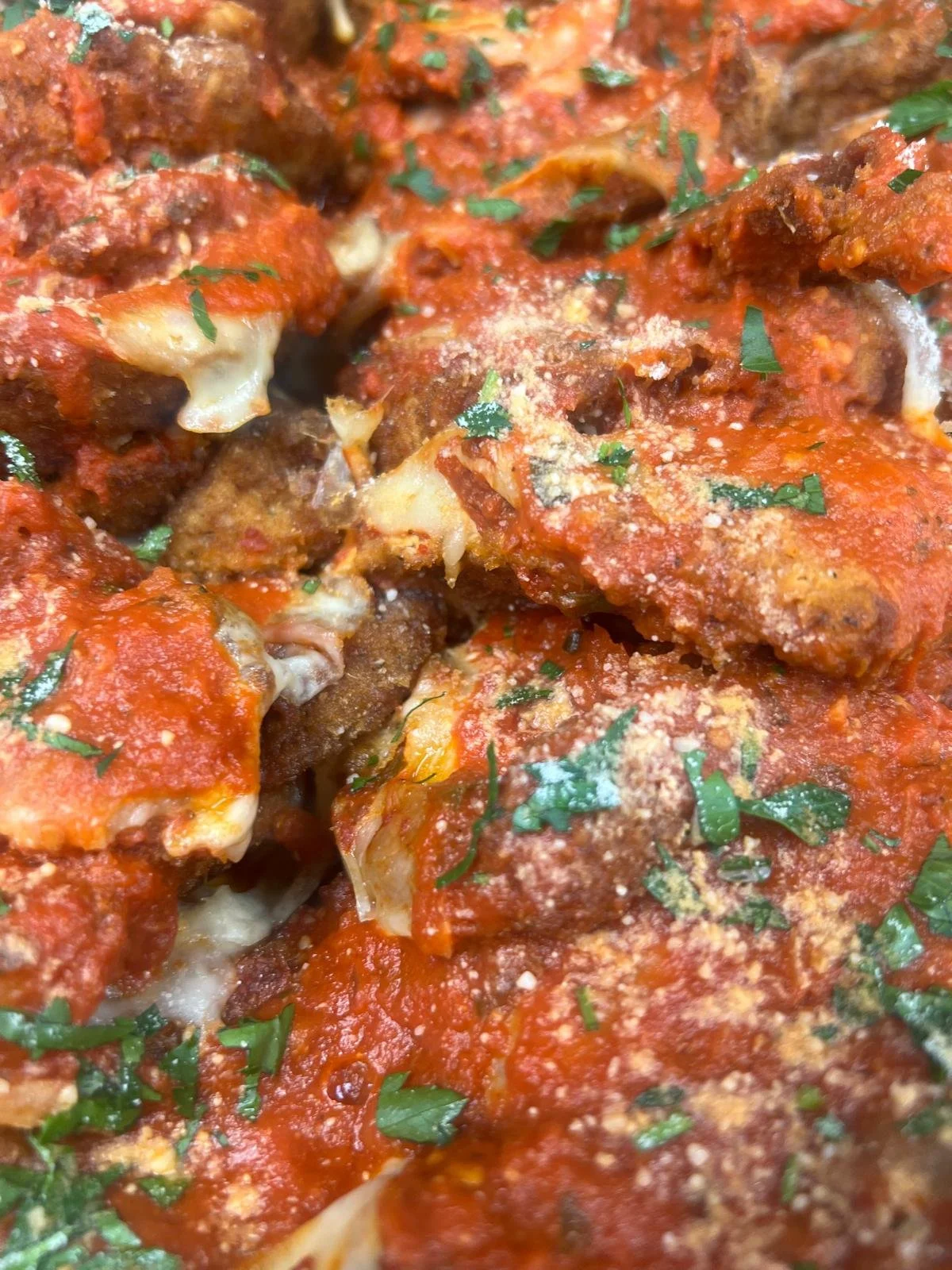 Close-up of baked Italian-style meatballs topped with tomato sauce, cheese, and chopped parsley.