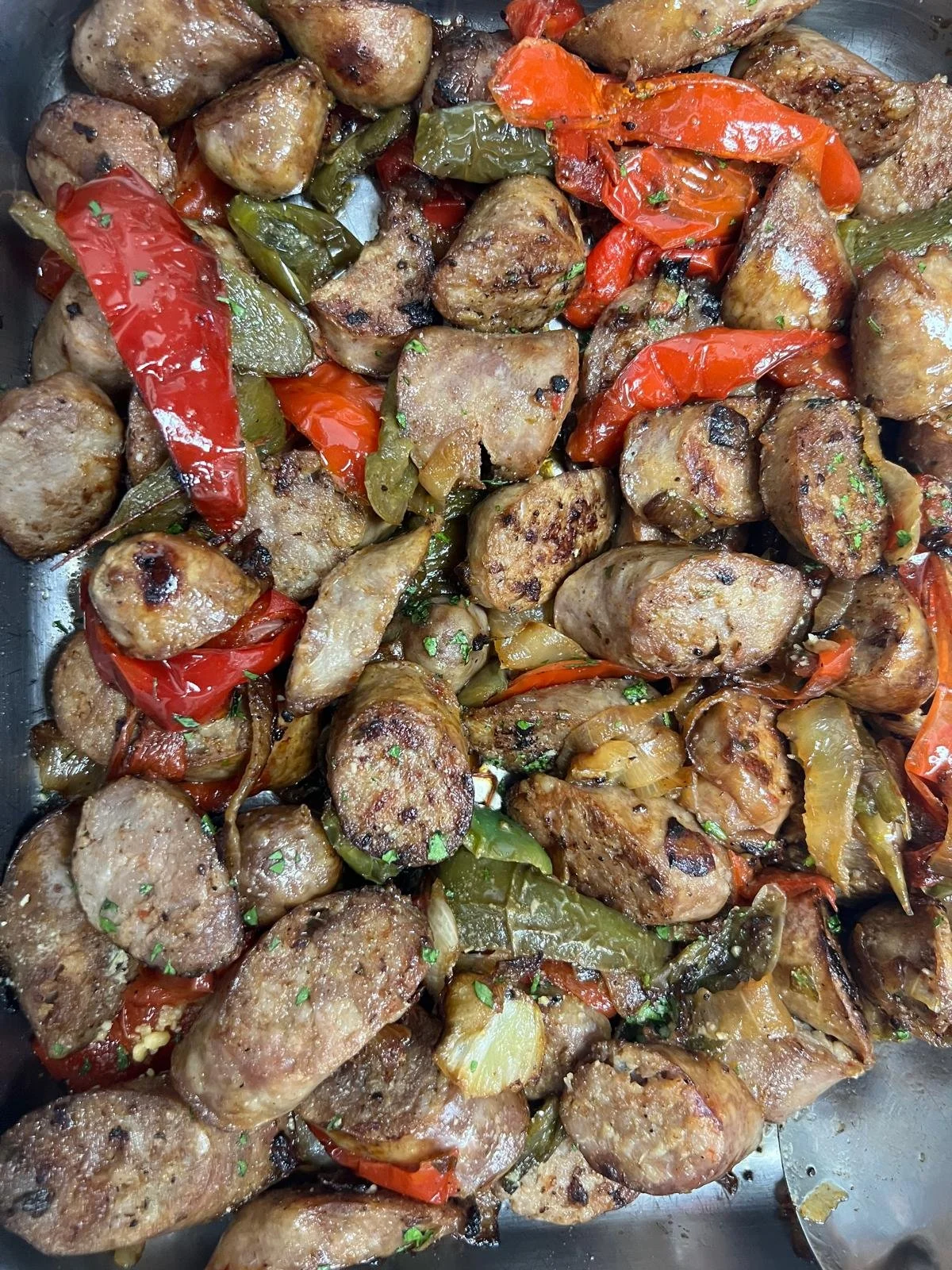 Cooked sausage links with roasted red, green, and yellow peppers, and onions.