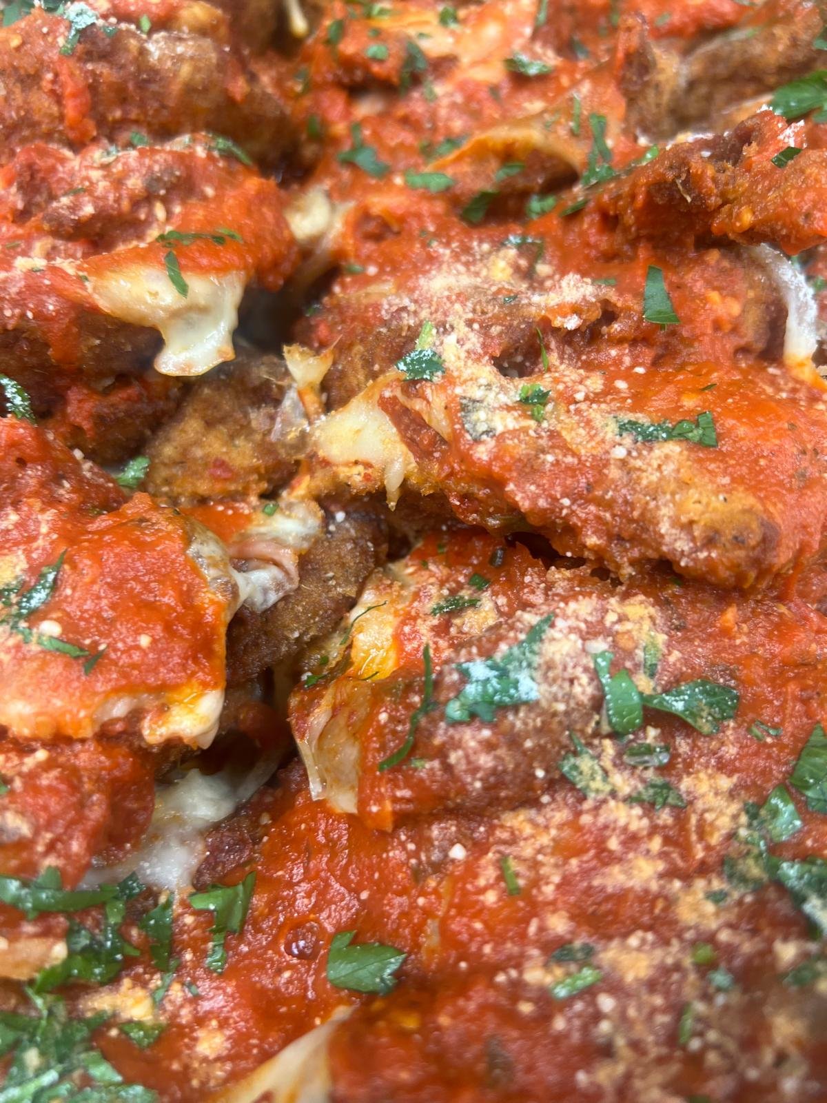Close-up of baked meatballs topped with tomato sauce, grated cheese, and chopped parsley.