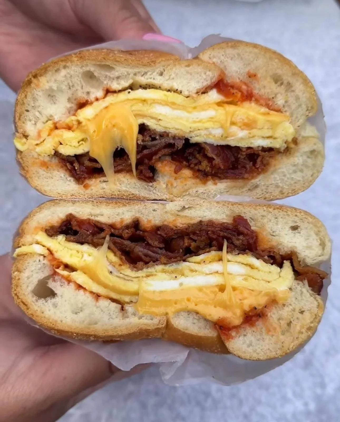 Close-up of a breakfast sandwich with scrambled eggs, bacon, and cheese inside a toasted hoagie bun.