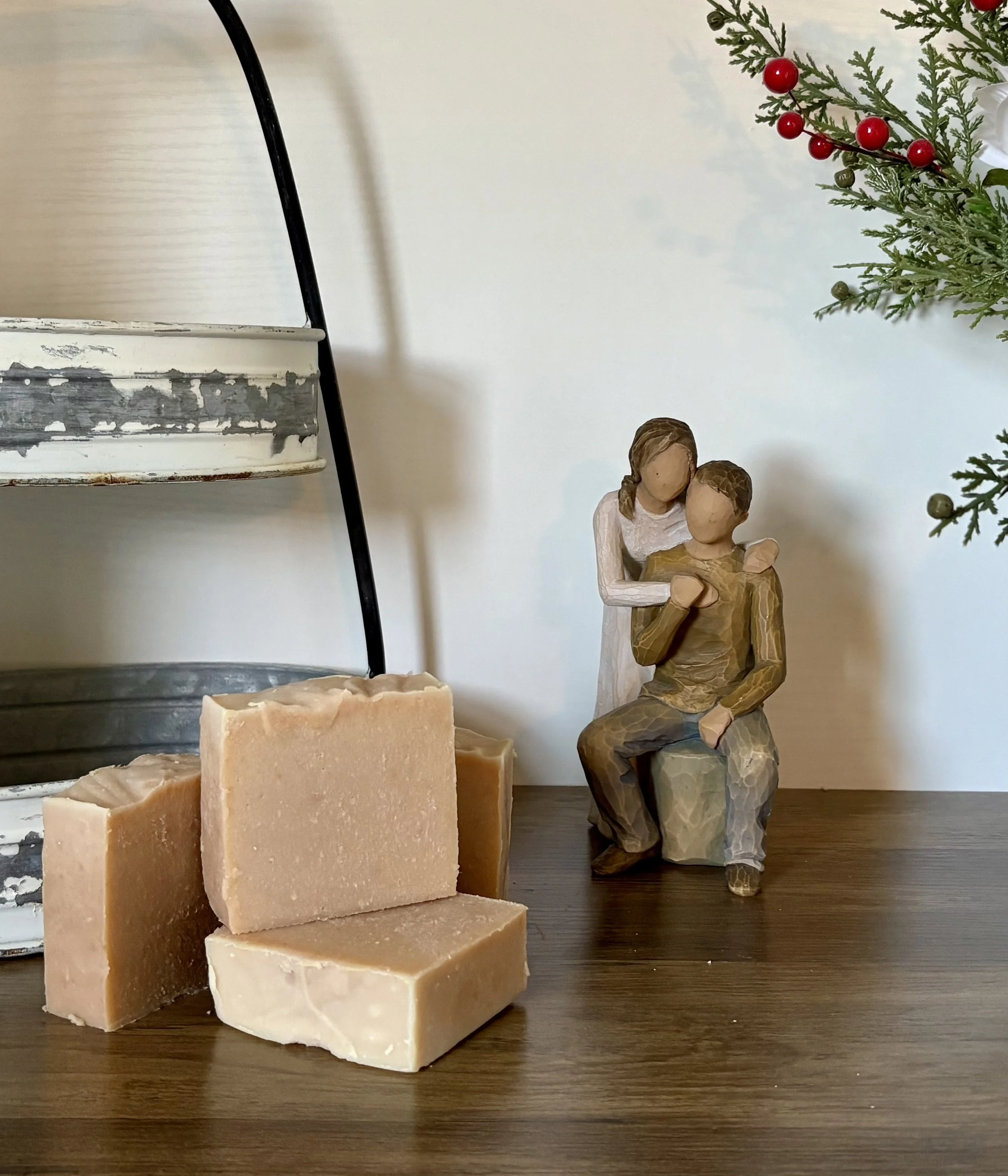 A decorative wooden figurine of a couple, with the woman embracing the man, placed on a wooden surface next to bars of soap and a metal shelf.