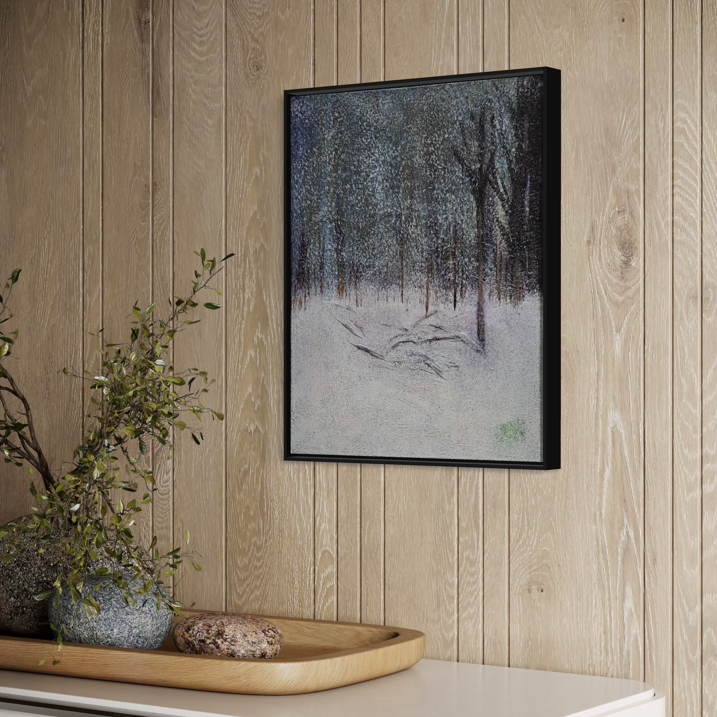 Framed painting of a snowy winter forest scene hung on wood-paneled wall, with a wooden tray holding rocks and plant in front.
