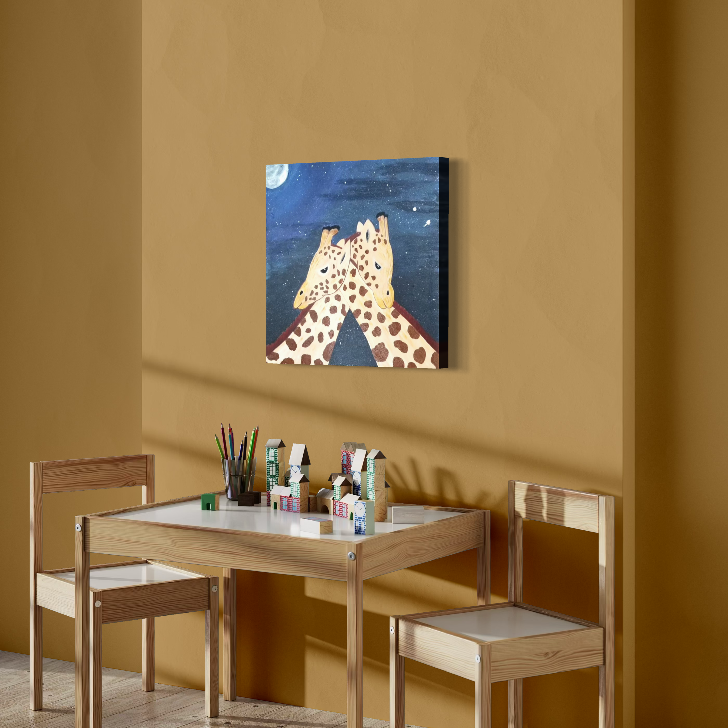 A wall with a painting of two giraffes with their heads touching under a starry night sky. A small table and two chairs are in front, decorated with building blocks, pencils, and small toys.