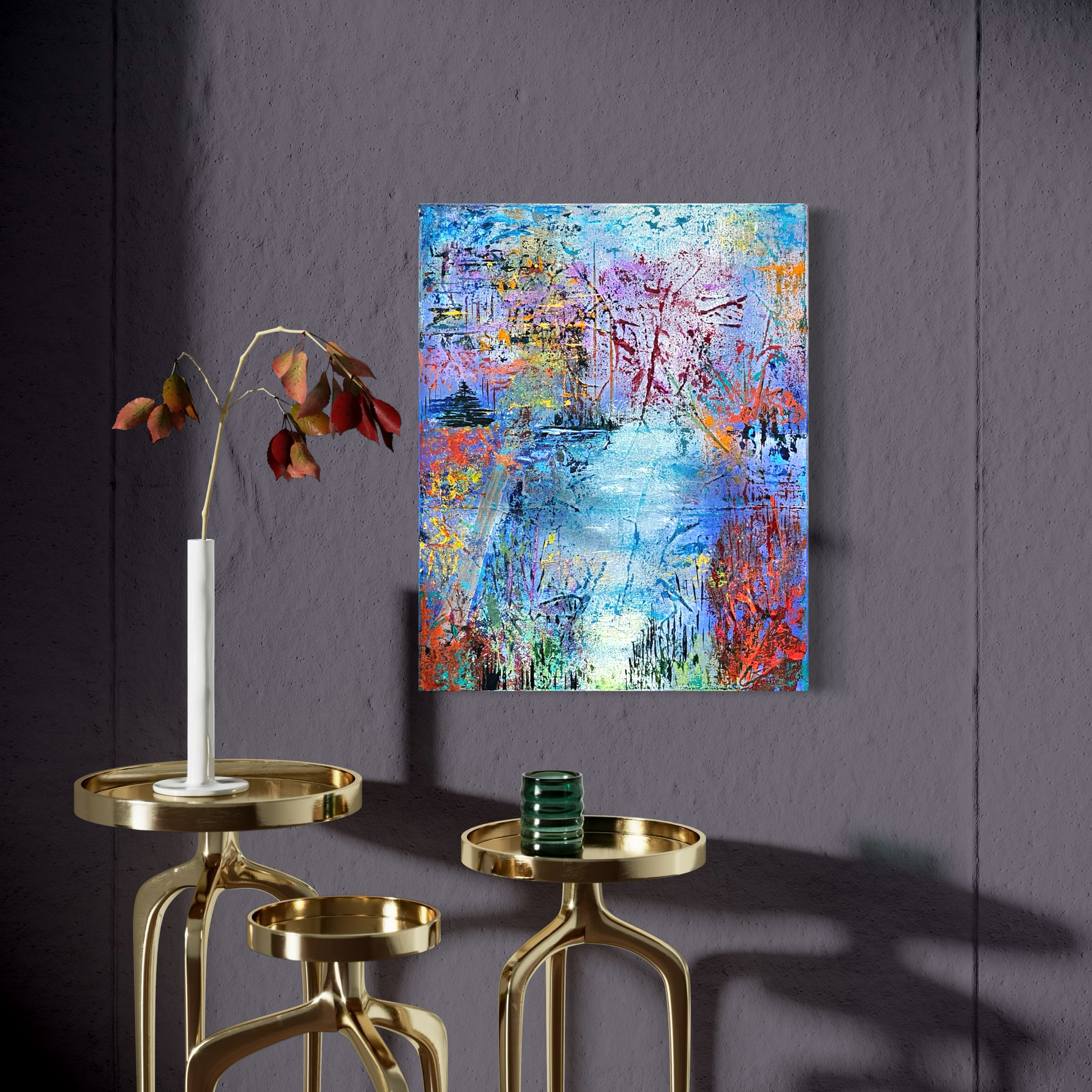 A colorful abstract painting hangs on a dark gray wall, with a white and red flower plant on a gold side table, and two other gold side tables with a green candle holder.