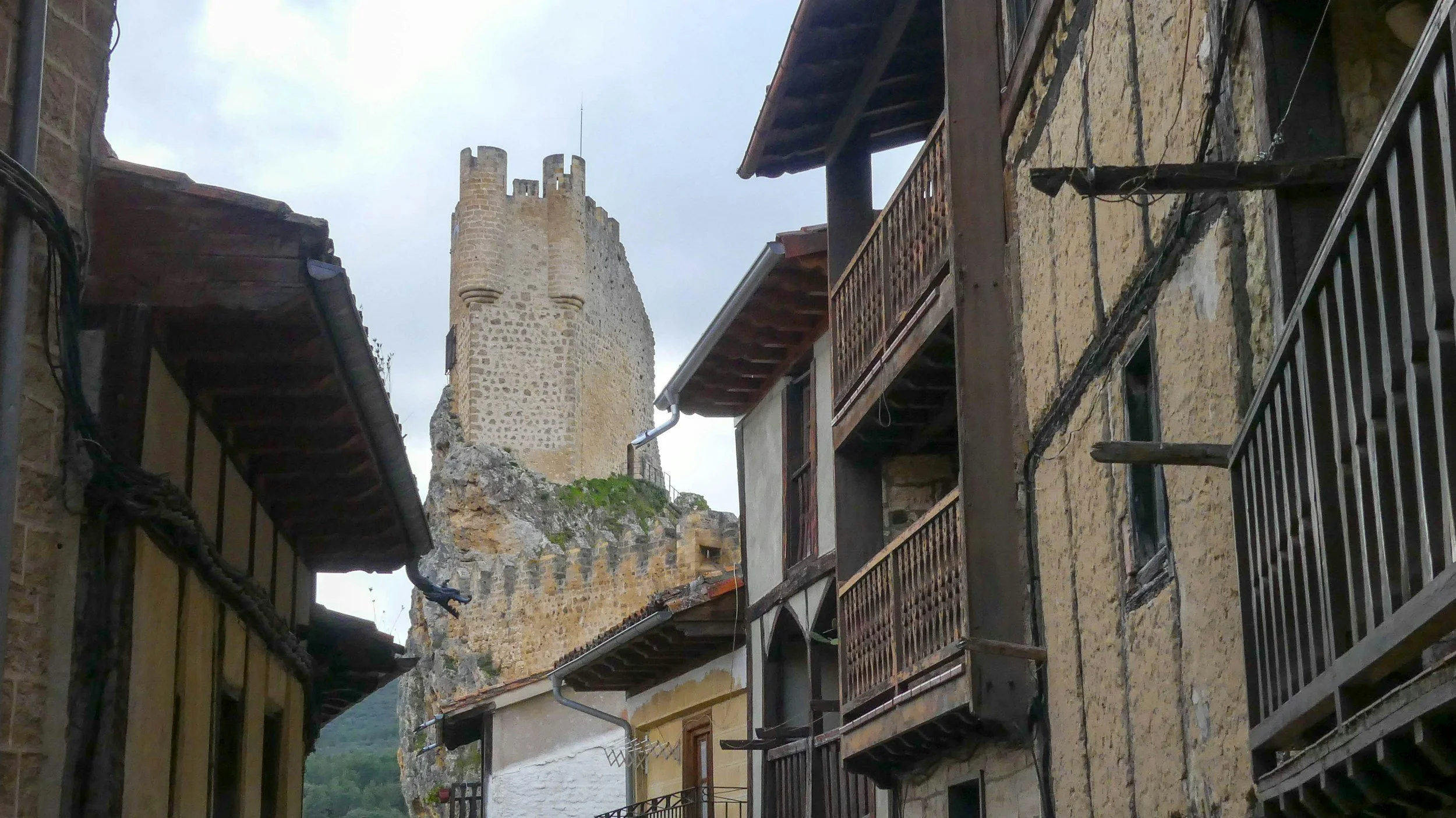 Vista de calle antigua con casas de madera y una torre de castillo en el fondo.