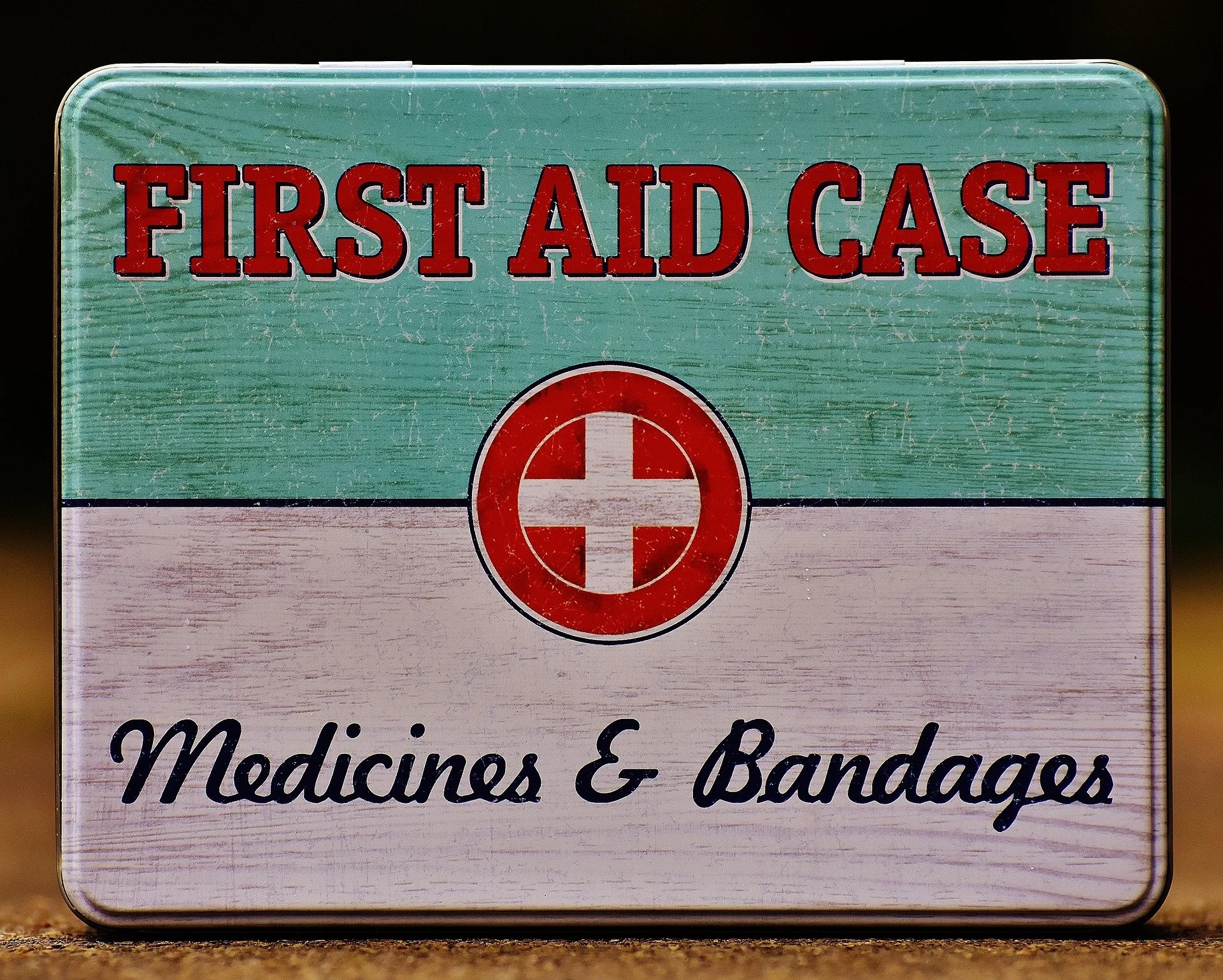 A vintage first aid kit box with the label 'First Aid Case' and 'Medicines & Bandages', featuring a red cross symbol in the center.