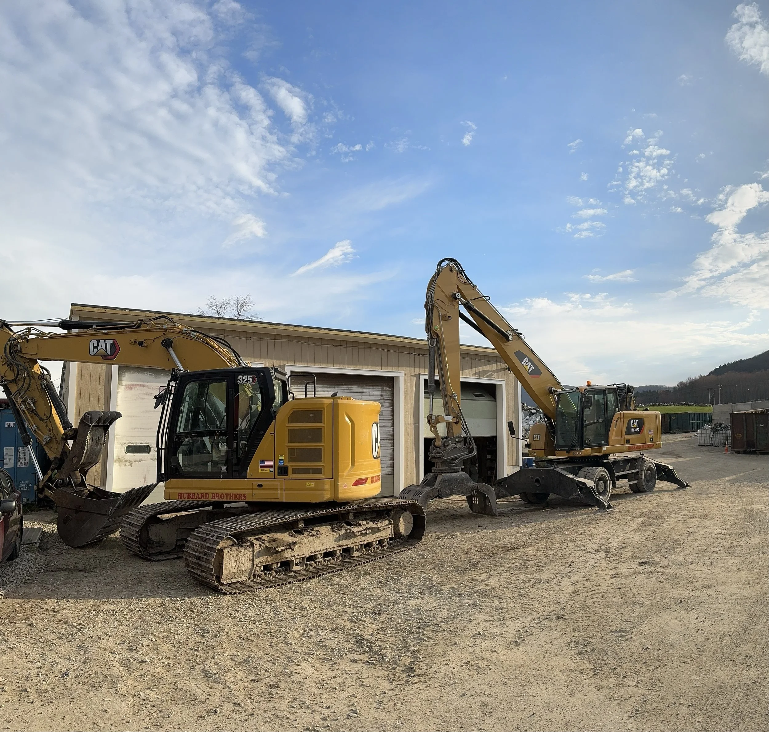 This image displays the excavator in front of the material handler, both parked in front of the garage. The excavator shown is used during demolition jobs.
