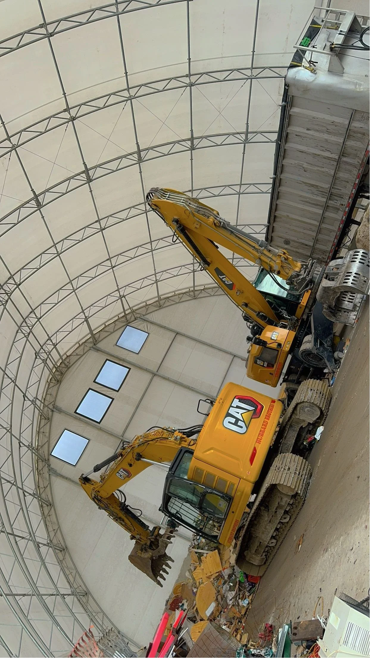 A yellow Caterpillar excavator working inside a large, partially constructed storage building with a metal framework and high windows.