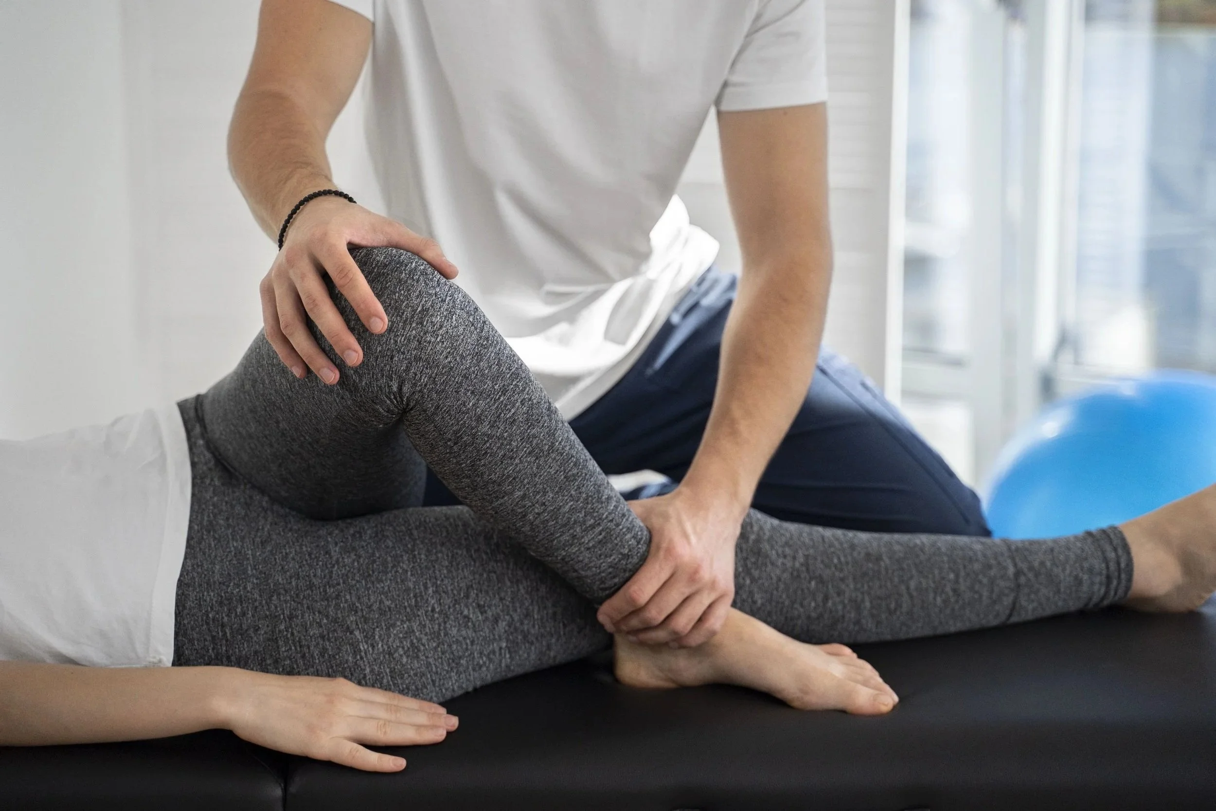 Ein Physiotherapeut führt eine Kniemobilisation an einer Patientin durch, die auf einer Behandlungsliege liegt.