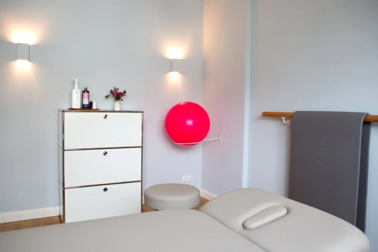 Ein heller, modern eingerichteter Behandlungsraum einer Physiotherapie- und Osteopathie-Praxis mit Therapieliege, Gymnastikball und ruhiger, freundlicher Atmosphäre.