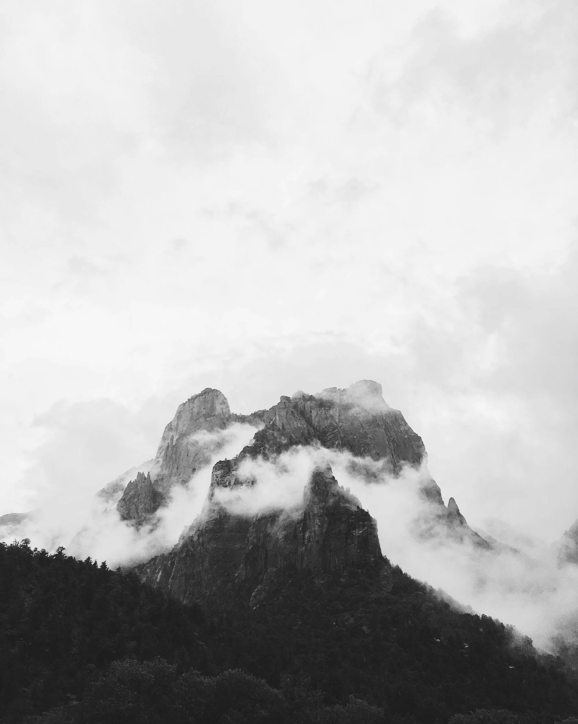 Black and white photograph of a mountain with clouds around its peak, surrounded by a forested landscape, representing advantage and achievement.