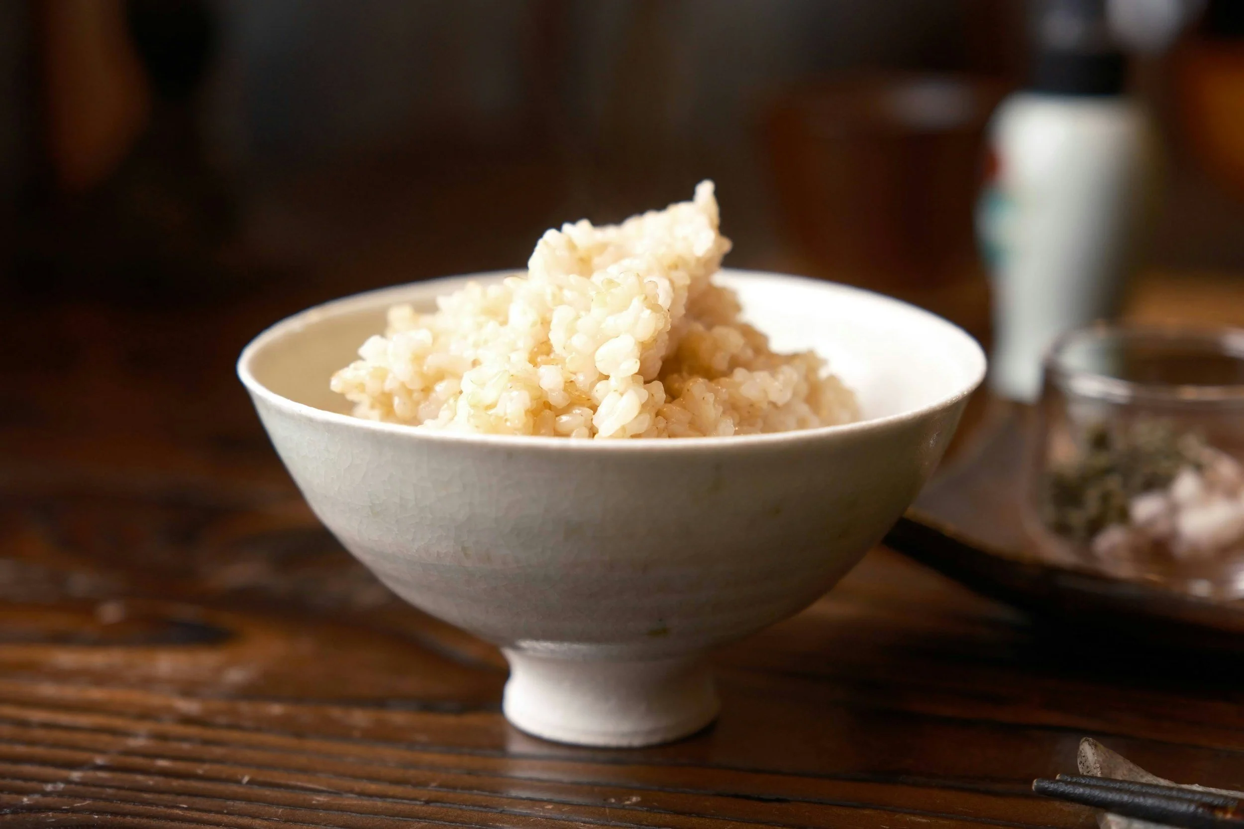 A white ceramic bowl filled with cooked rice on a wooden table