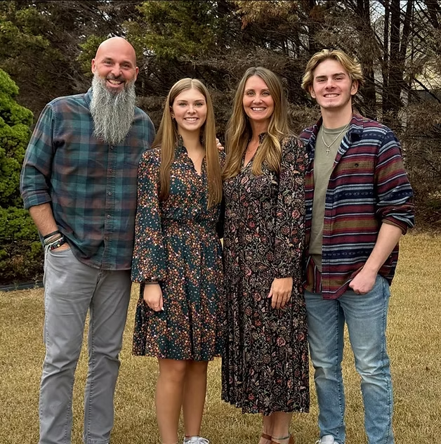A group of four people, two men and two women, standing outdoors in front of trees, smiling at the camera.